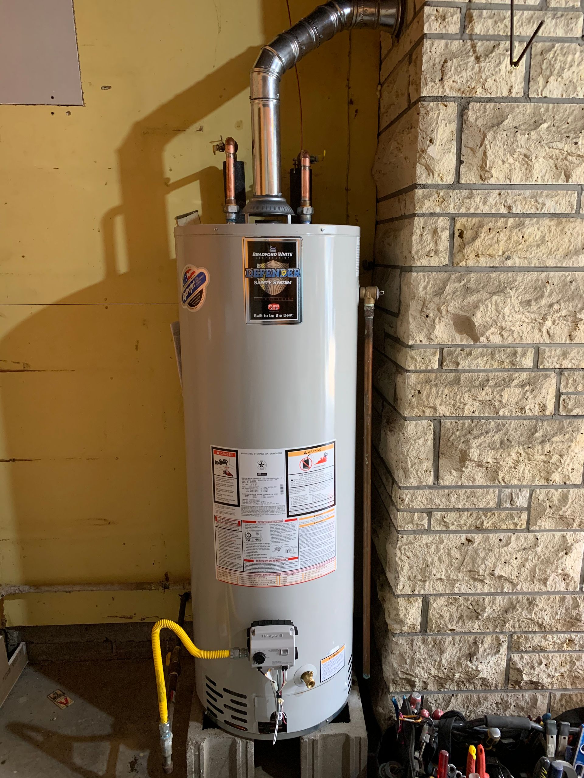 White water heater with vent pipe in a basement utility area beside a stone wall.