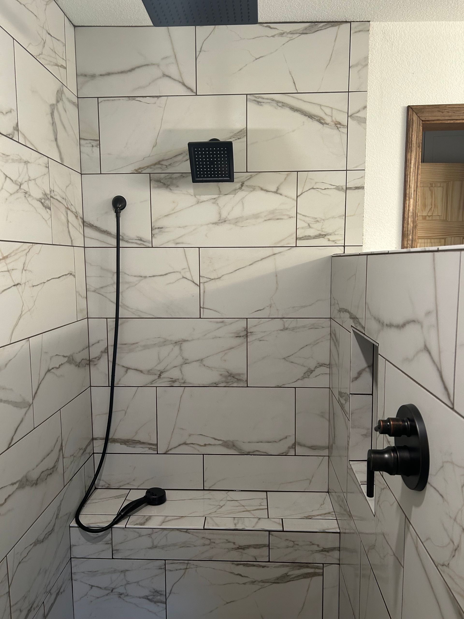 Marble-tiled shower stall with black fixtures and handheld showerhead, no door visible