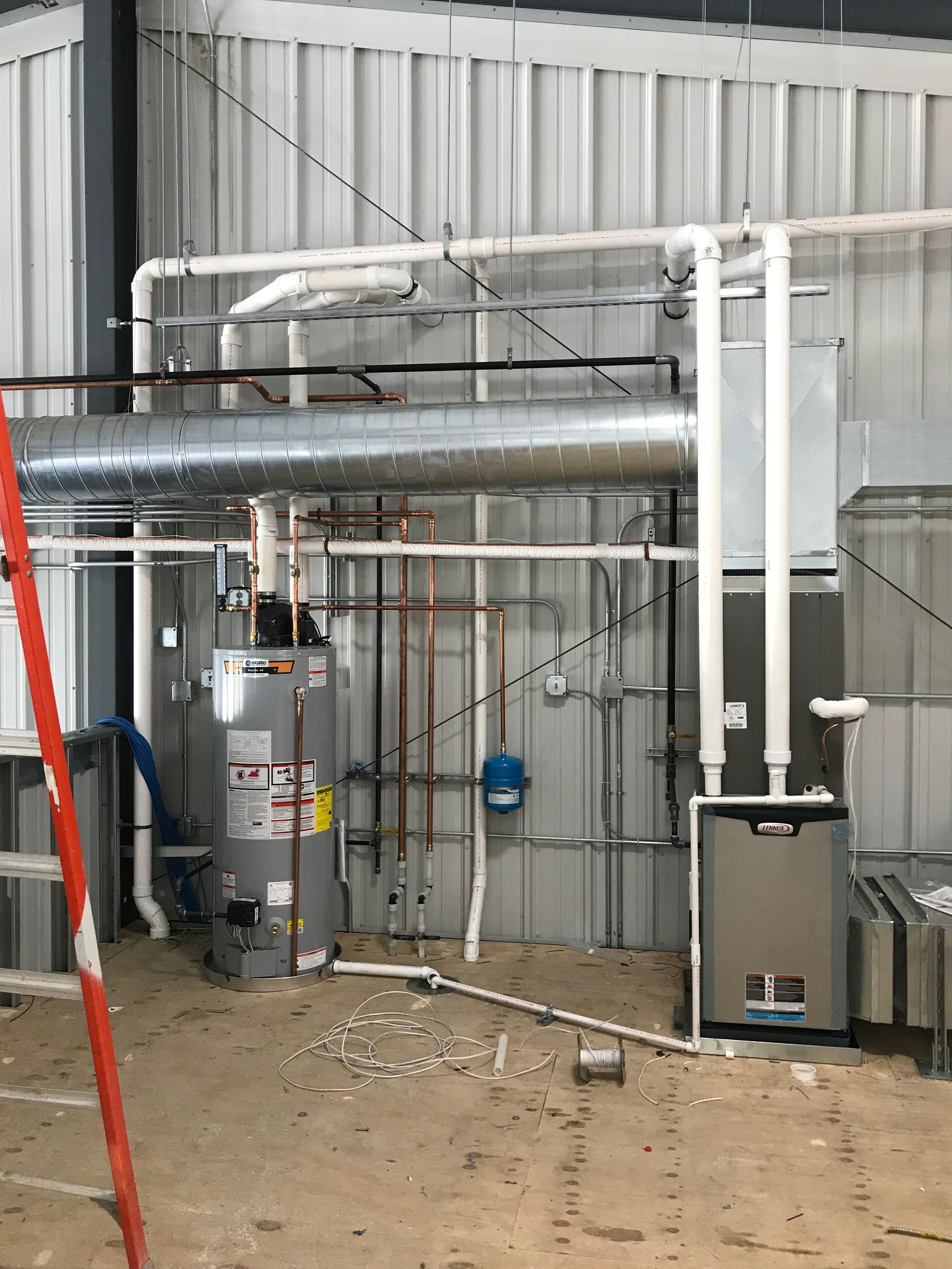 Industrial machinery and ductwork inside a metal-walled utility room, with pipes, tanks, and equipment on a dirt floor