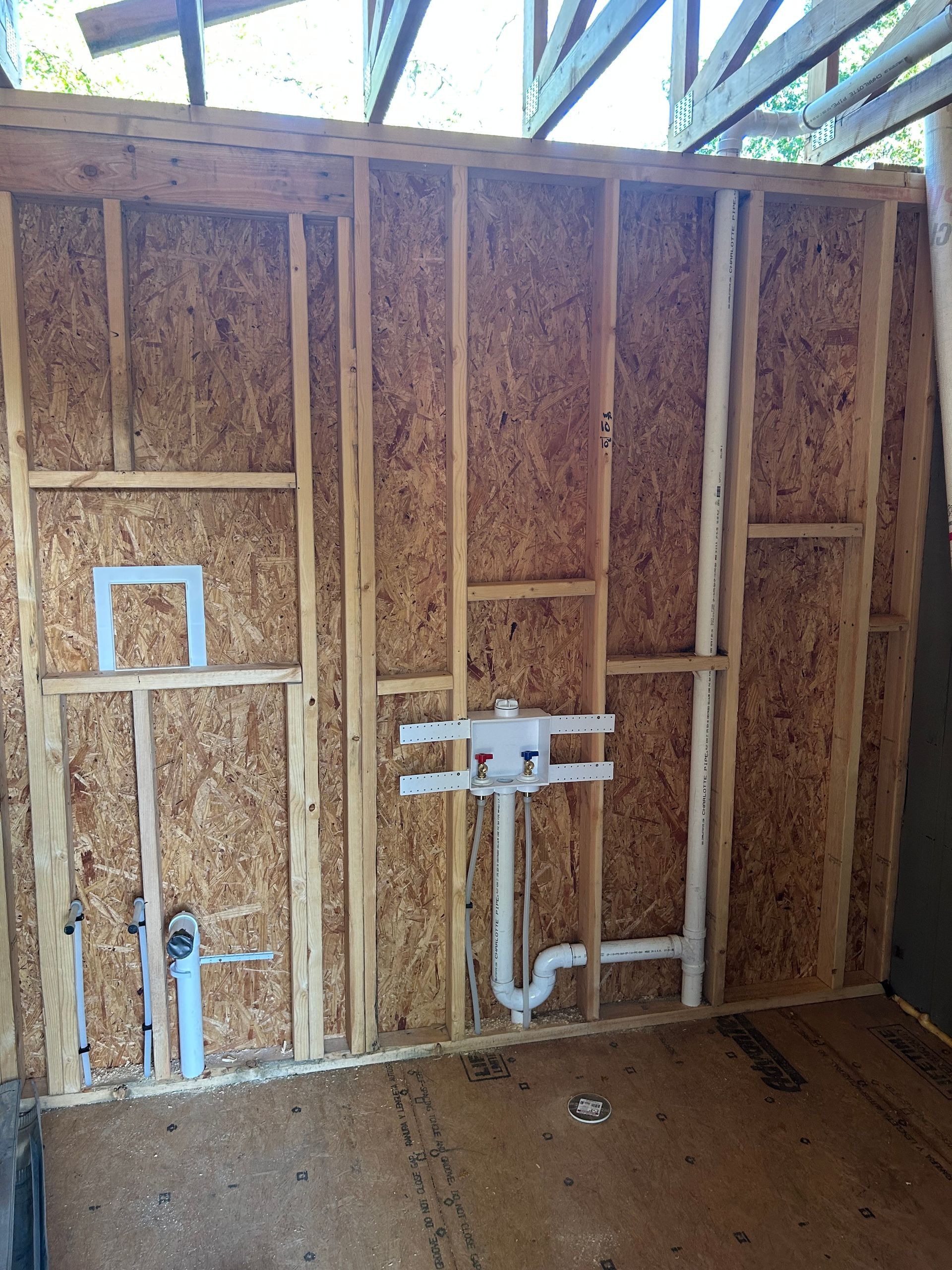 Unfinished bathroom wall with exposed framing, installed shower plumbing, and a small window opening.