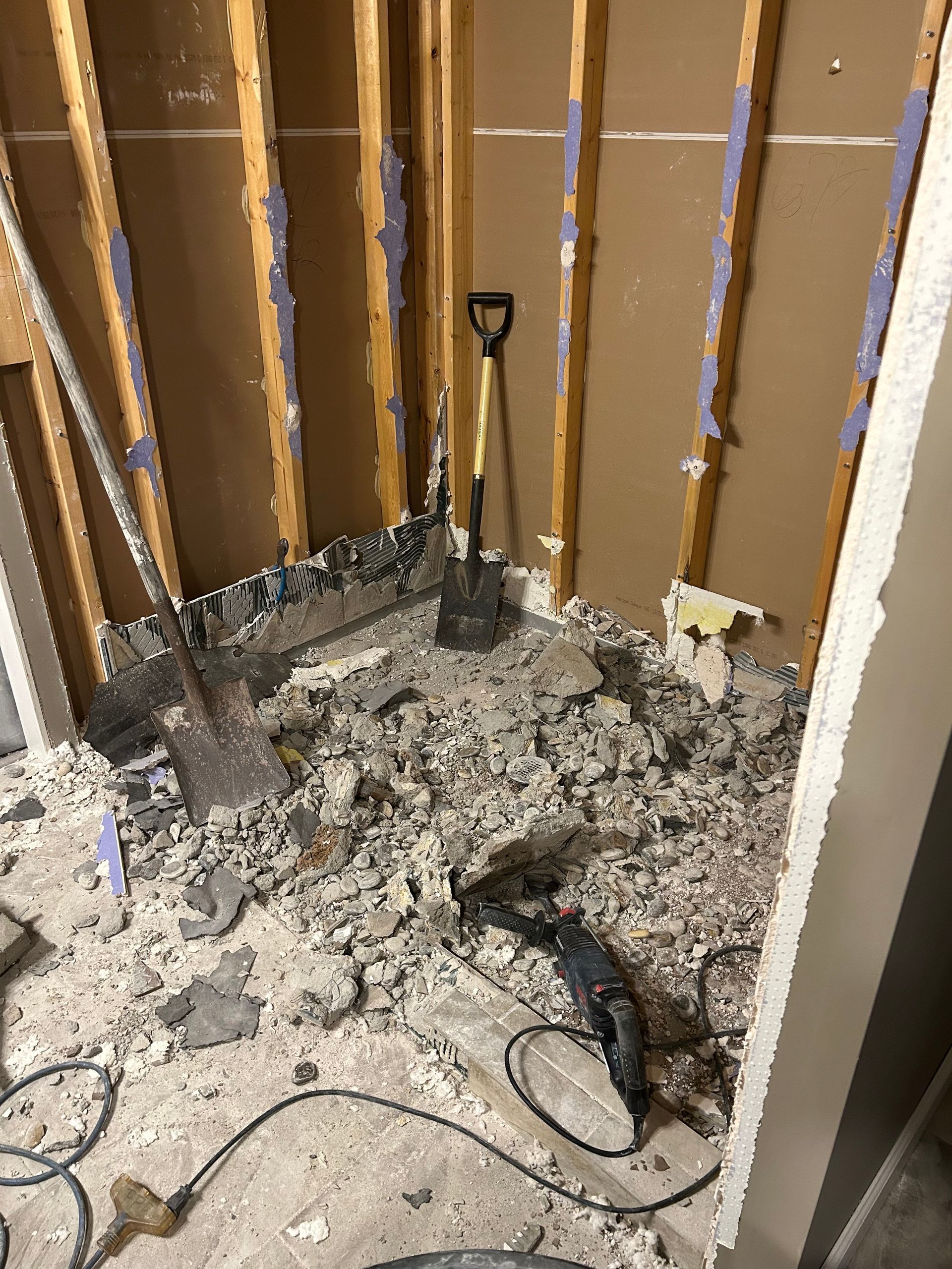 Damaged room interior with exposed wall studs, debris on the floor, and tools scattered around.