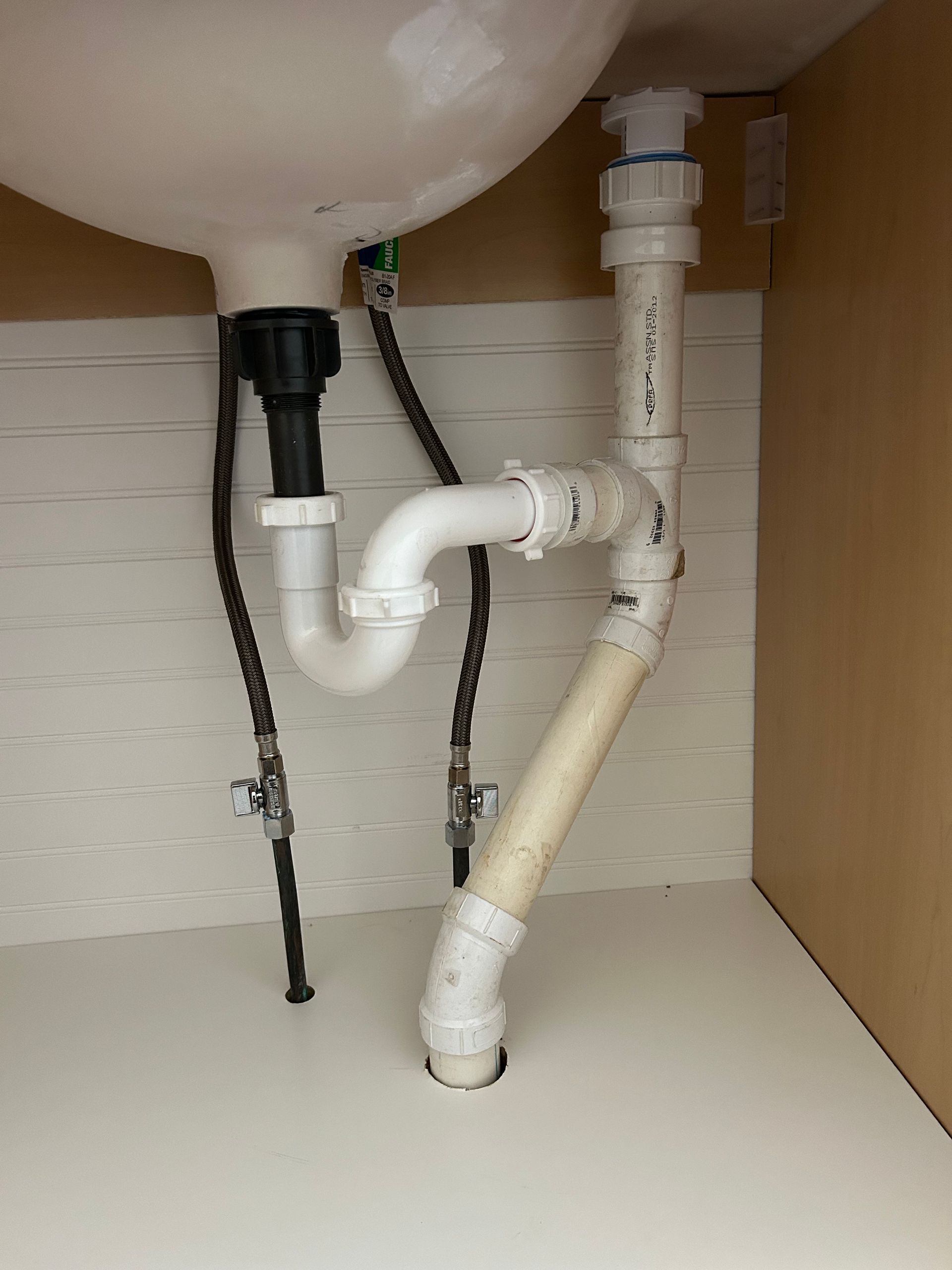 Technician inspecting plumbing under a sink with tools in a cabinet.