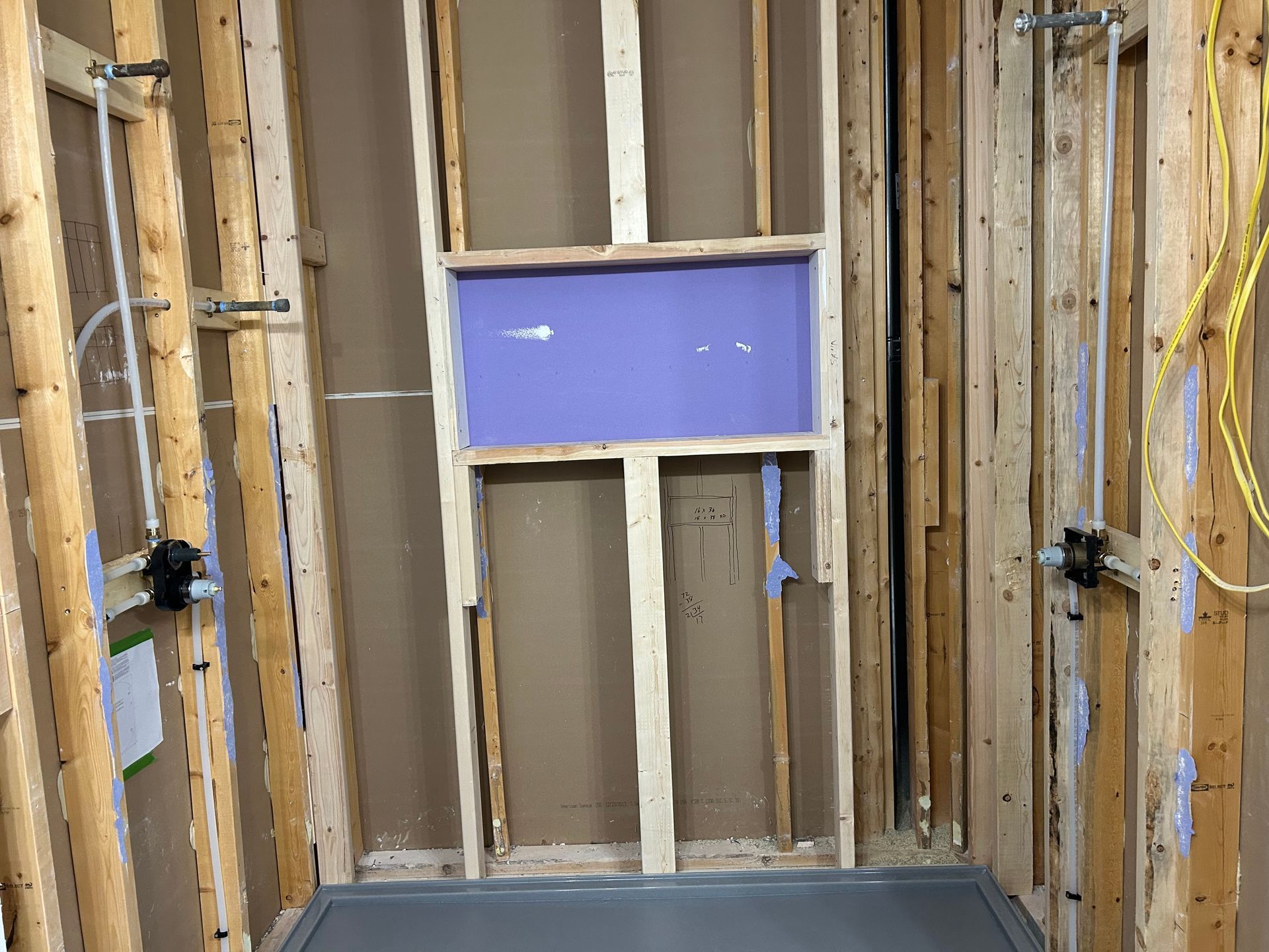 Unfinished wall framing with exposed studs and a blue insulation board section around a window opening.