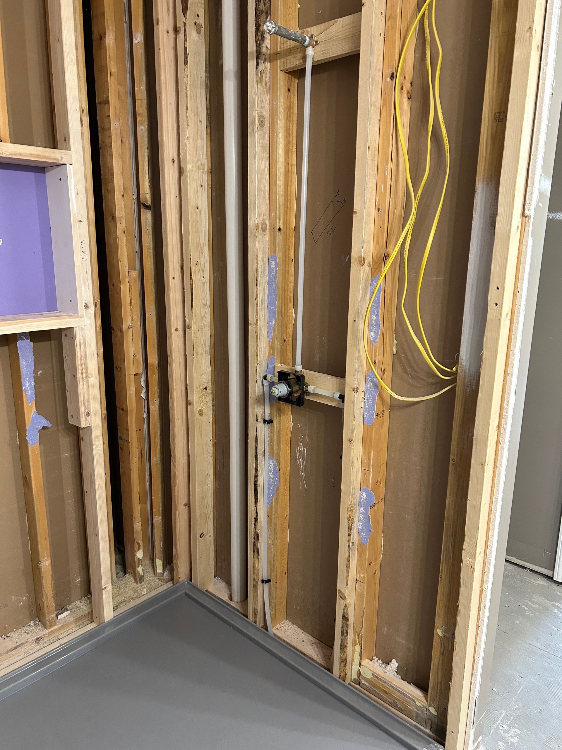 Exposed wall framing with wiring and plumbing in a partially renovated room with gray floor trim