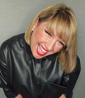 A woman wearing a black leather shirt and red lipstick is smiling.