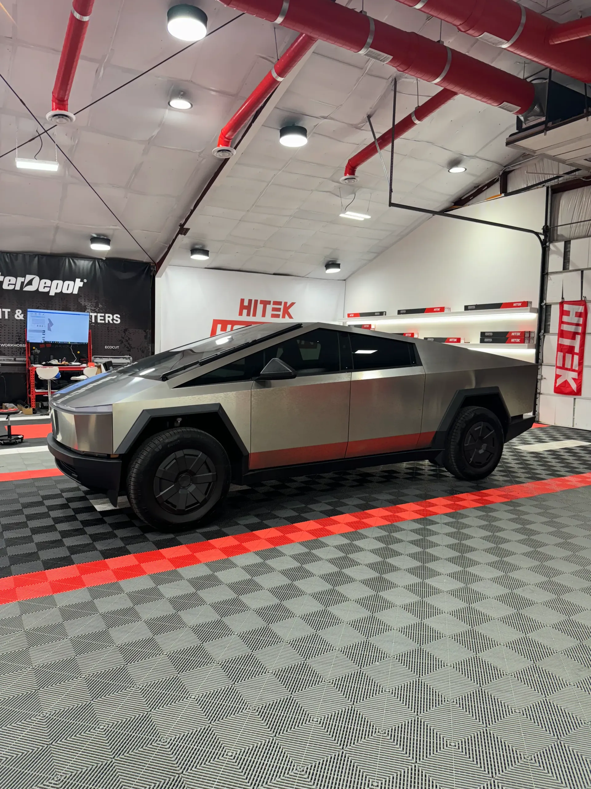 Tesla Cybertruck in a garage, with a red stripe along the side, and red pipes on the ceiling.