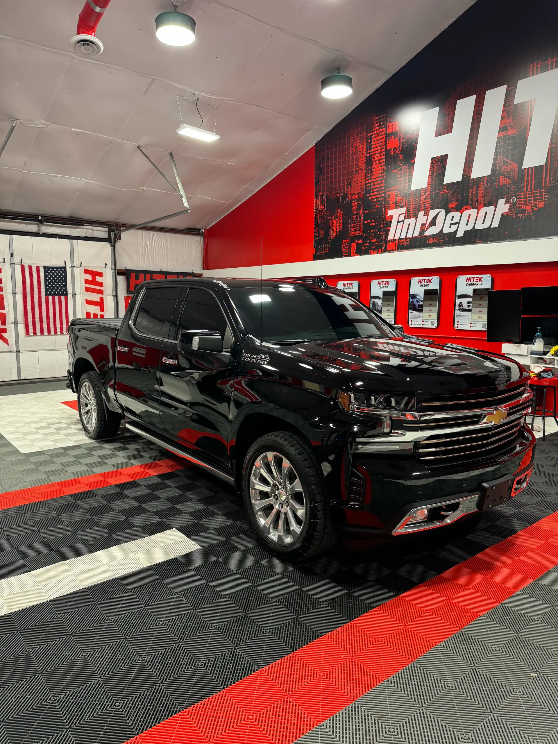 Black Chevrolet pickup truck in a shop with red and black flooring and wall graphics.