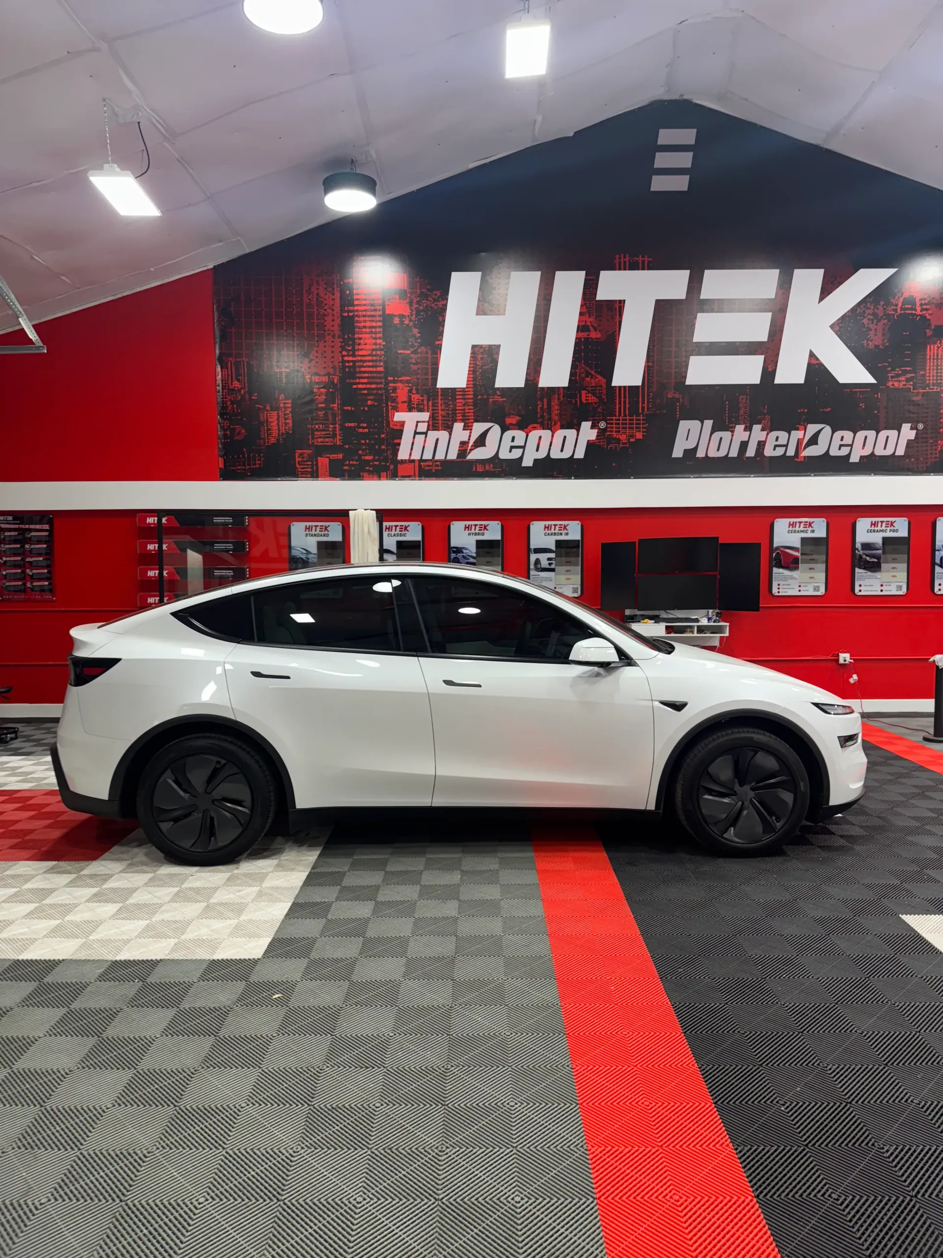 White Tesla SUV in a shop with red accents and the HiTek Tint Depot logo.