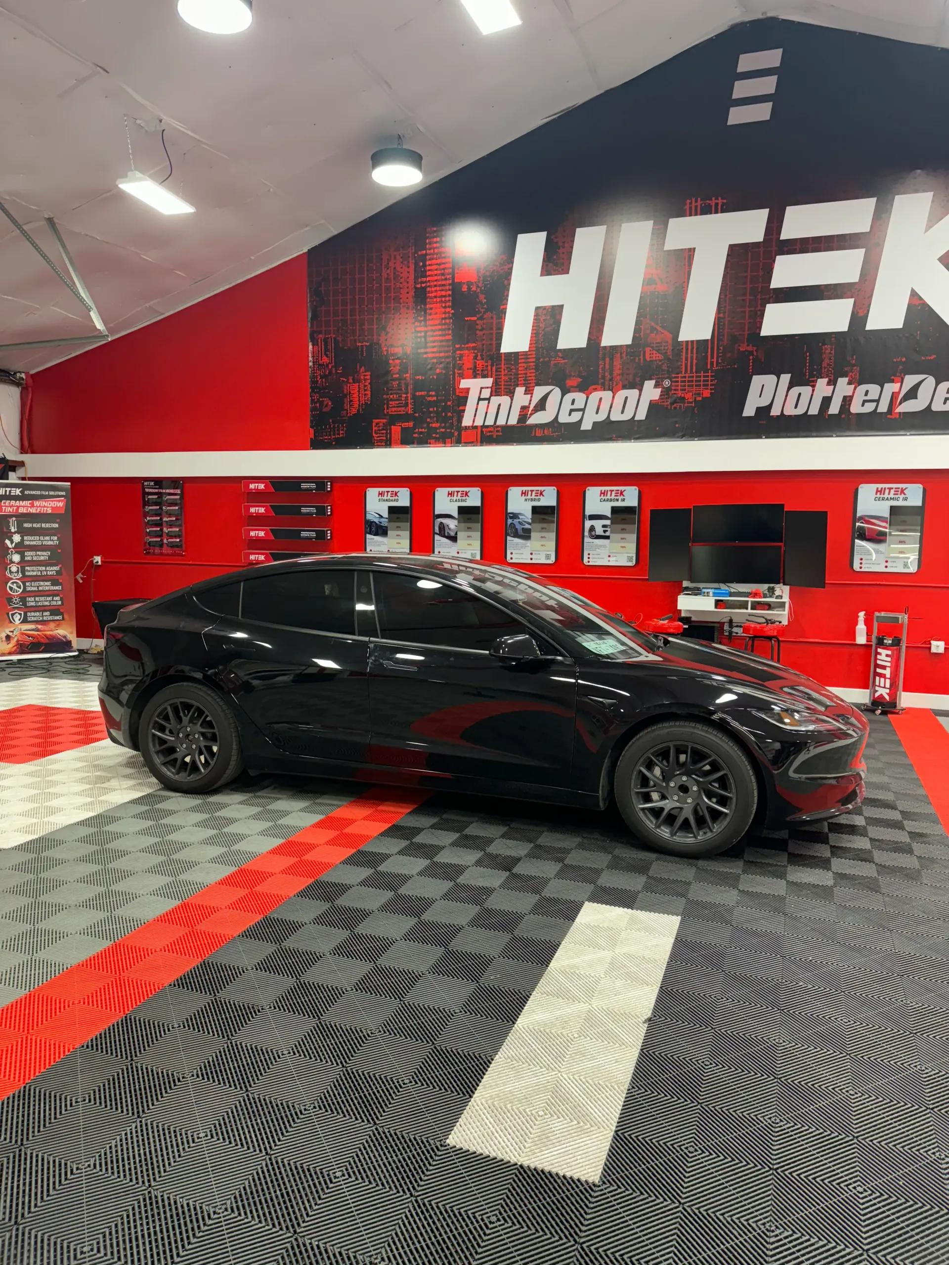 Black car in a shop with red and black flooring, with a 