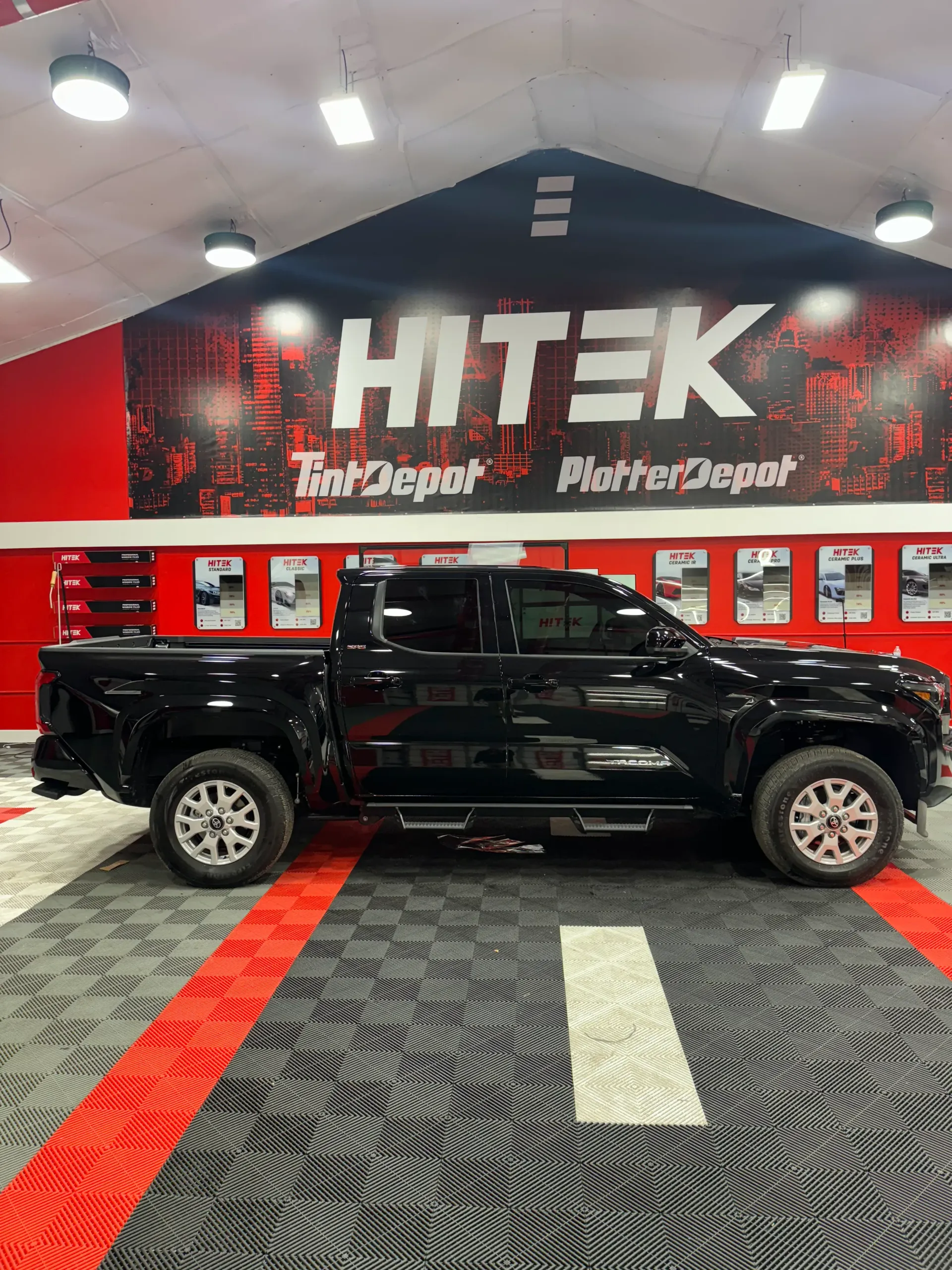 Black pickup truck parked inside a tint and repair shop with logo.
