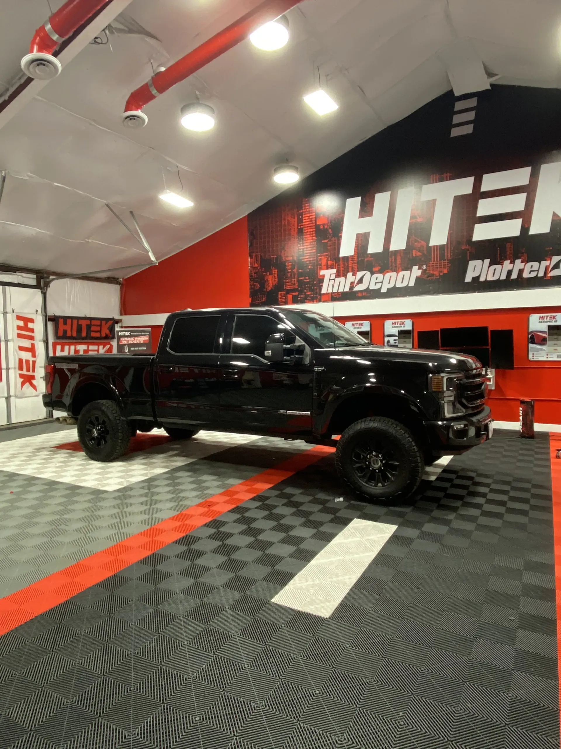 Black pickup truck parked in front of a red and white sign for Hitek Tint Depot.