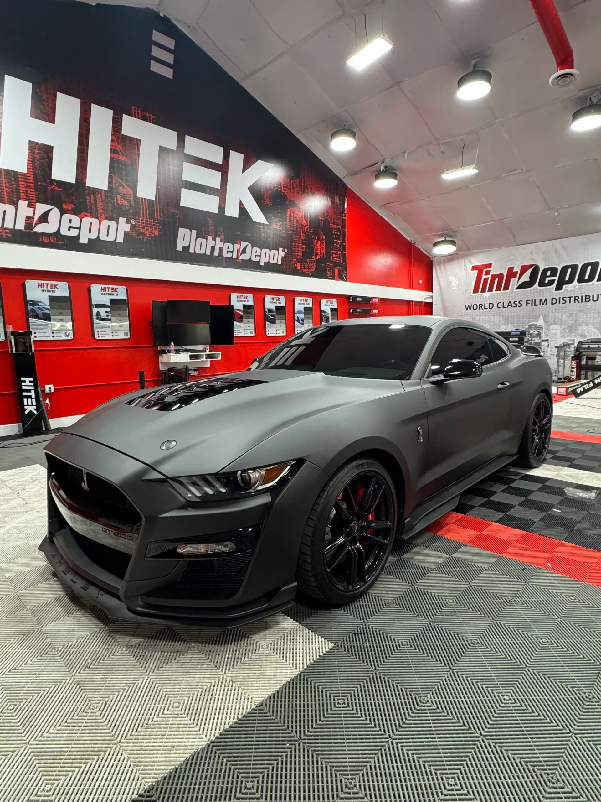 Gray matte Ford Mustang in a shop with Tint Depot signage.
