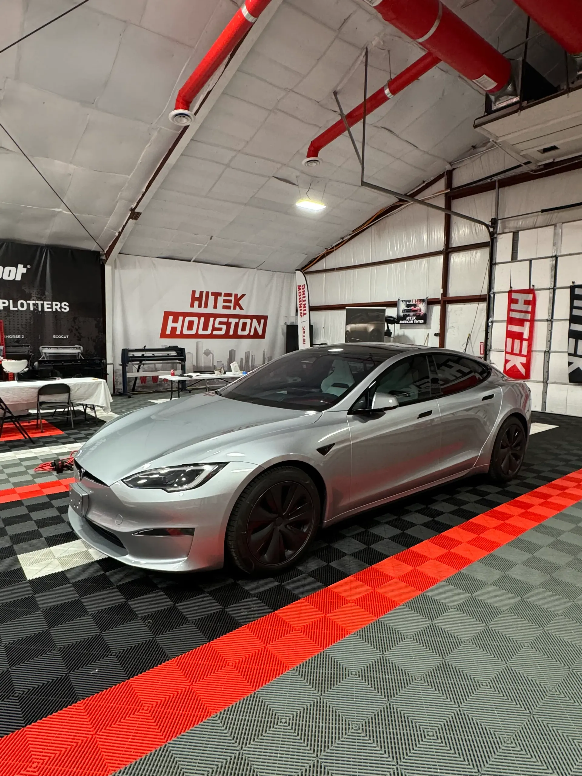 Silver Tesla Model S in a garage with red and black flooring, under the 