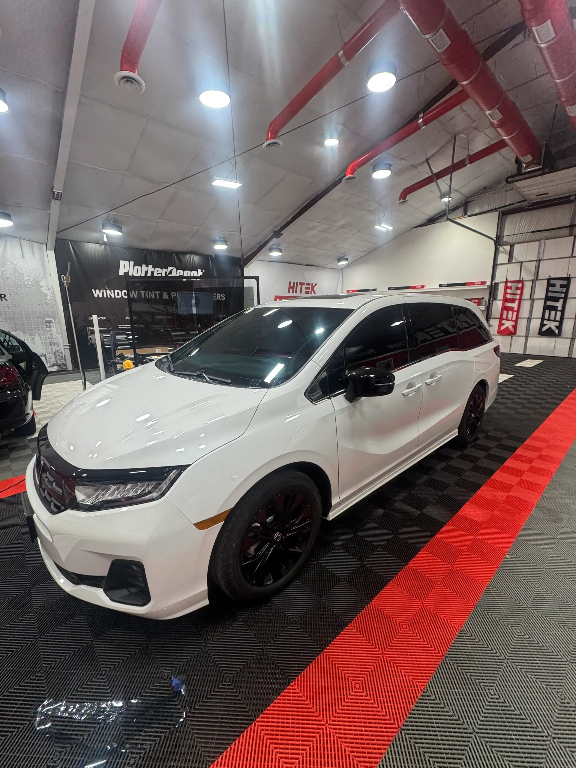 White Honda Odyssey minivan with black accents parked inside a brightly lit garage.