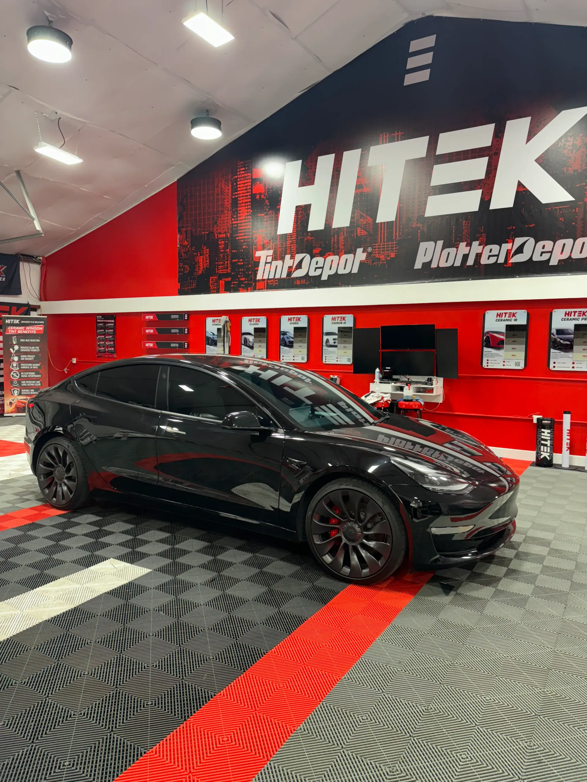 Black Tesla car with tinted windows inside a tint shop with red and black accents.