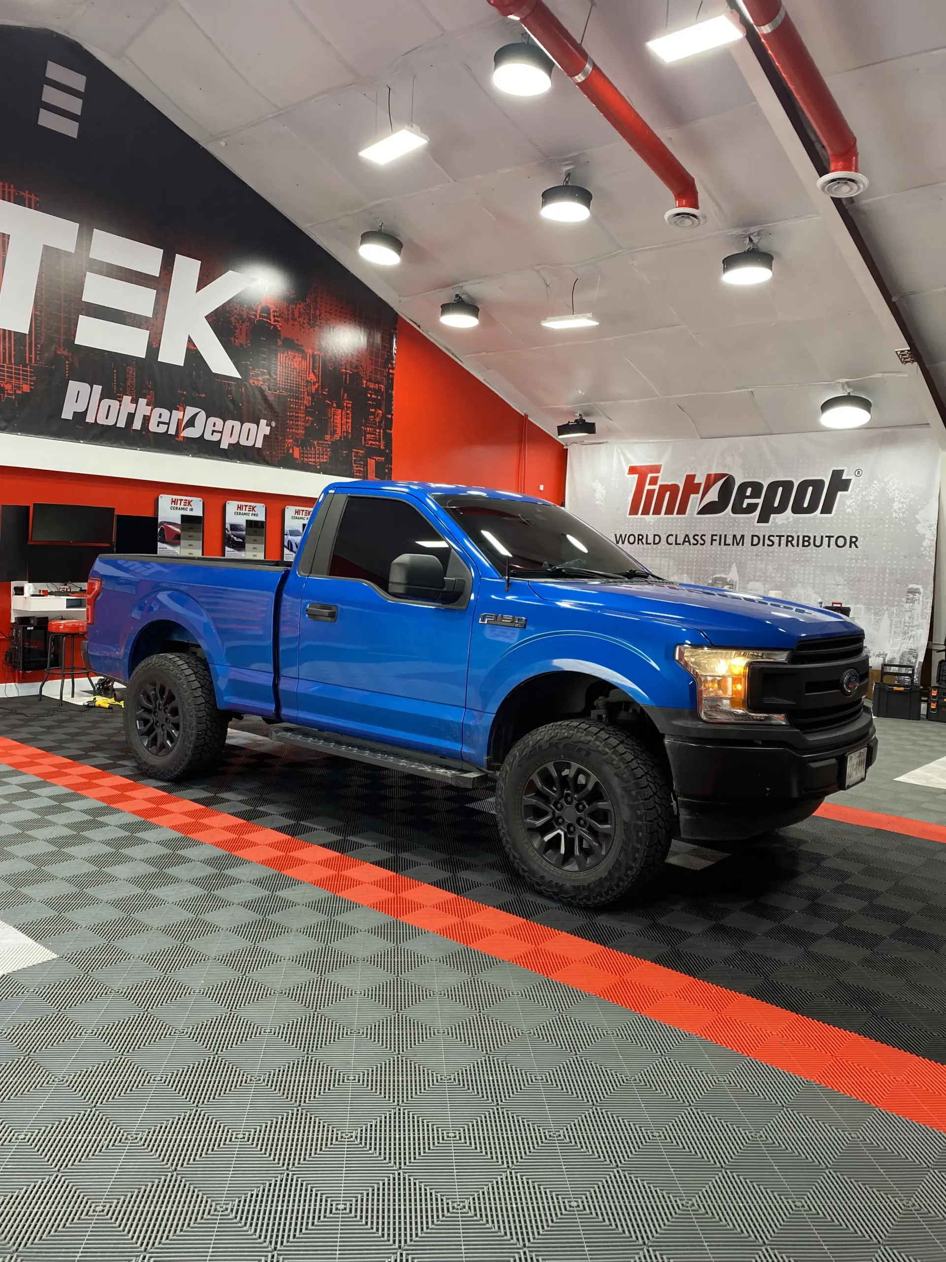 Blue Ford F-150 pickup truck in a shop with tinted windows and black wheels.