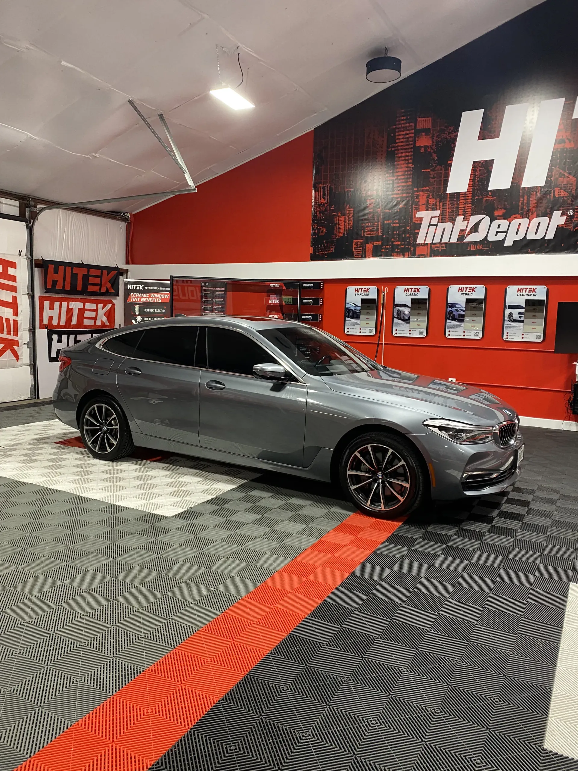 Gray BMW 6 Series Gran Turismo in a shop with red accents, likely for window tinting.