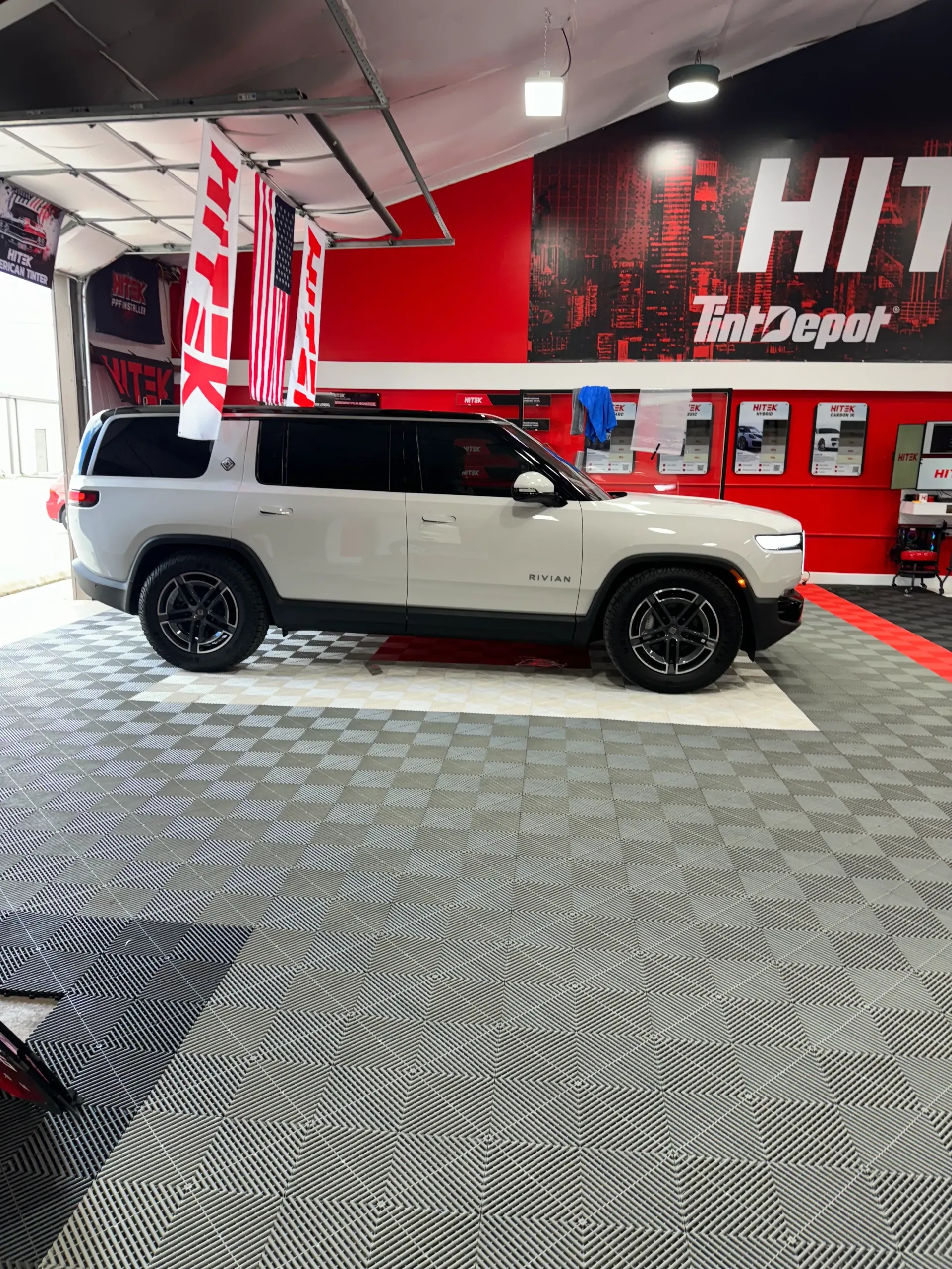 White SUV parked in a shop with red accents, black wheels, and checkered floor.