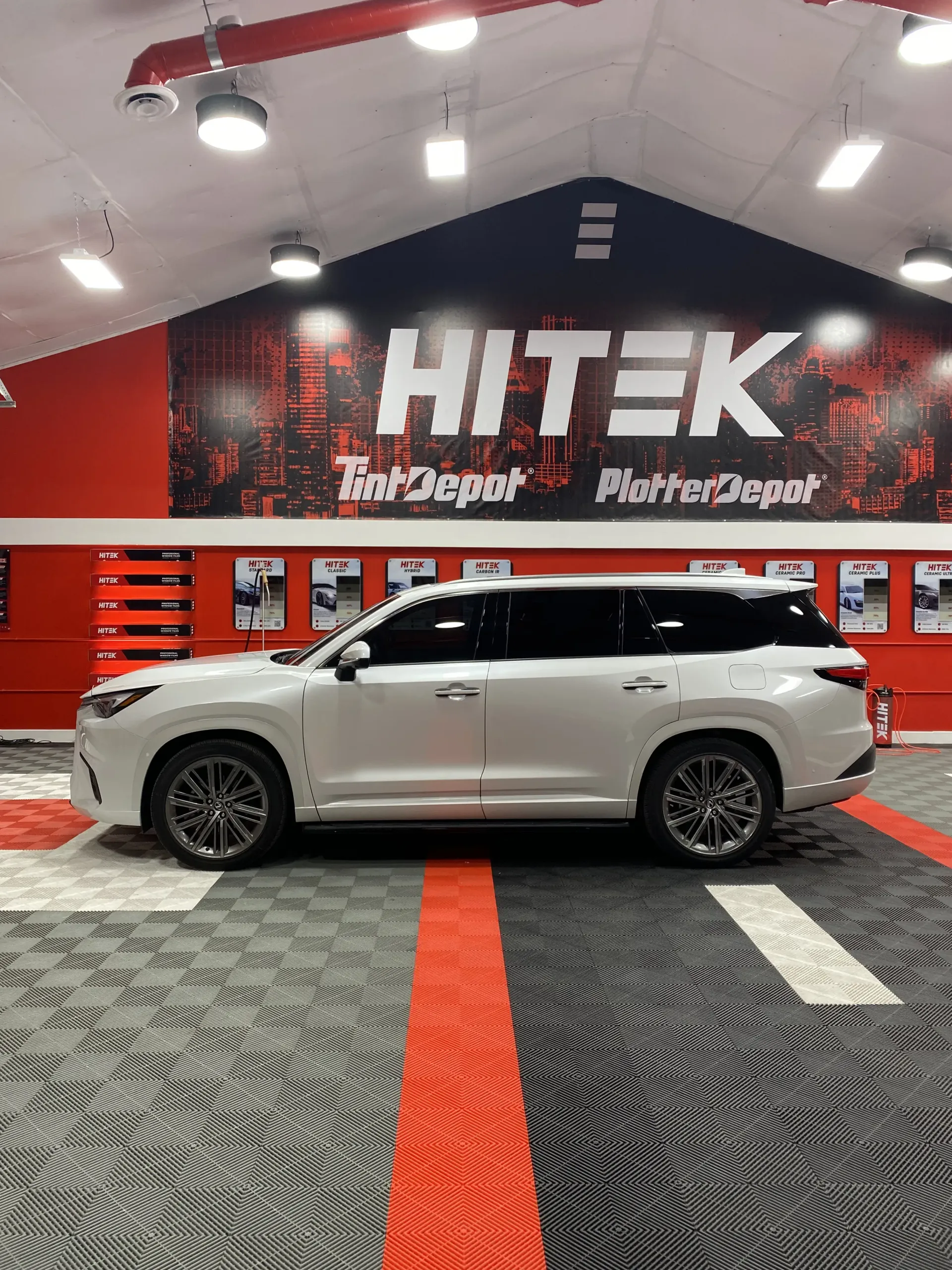 White SUV in a garage with red and black accents and a Hitek Tow Depot sign.