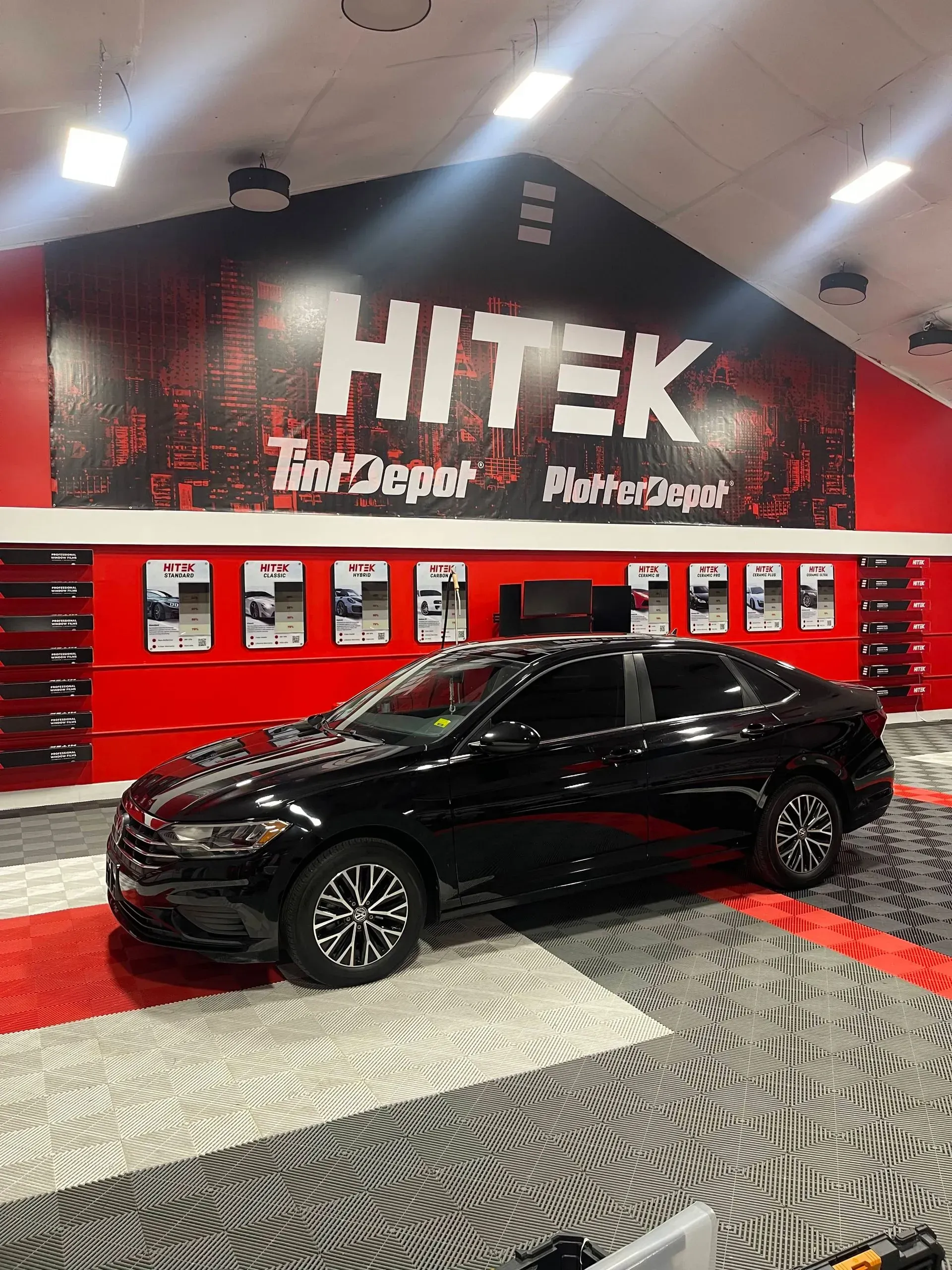 Black car parked in a HiTek Auto Depot showroom with red and gray decor.