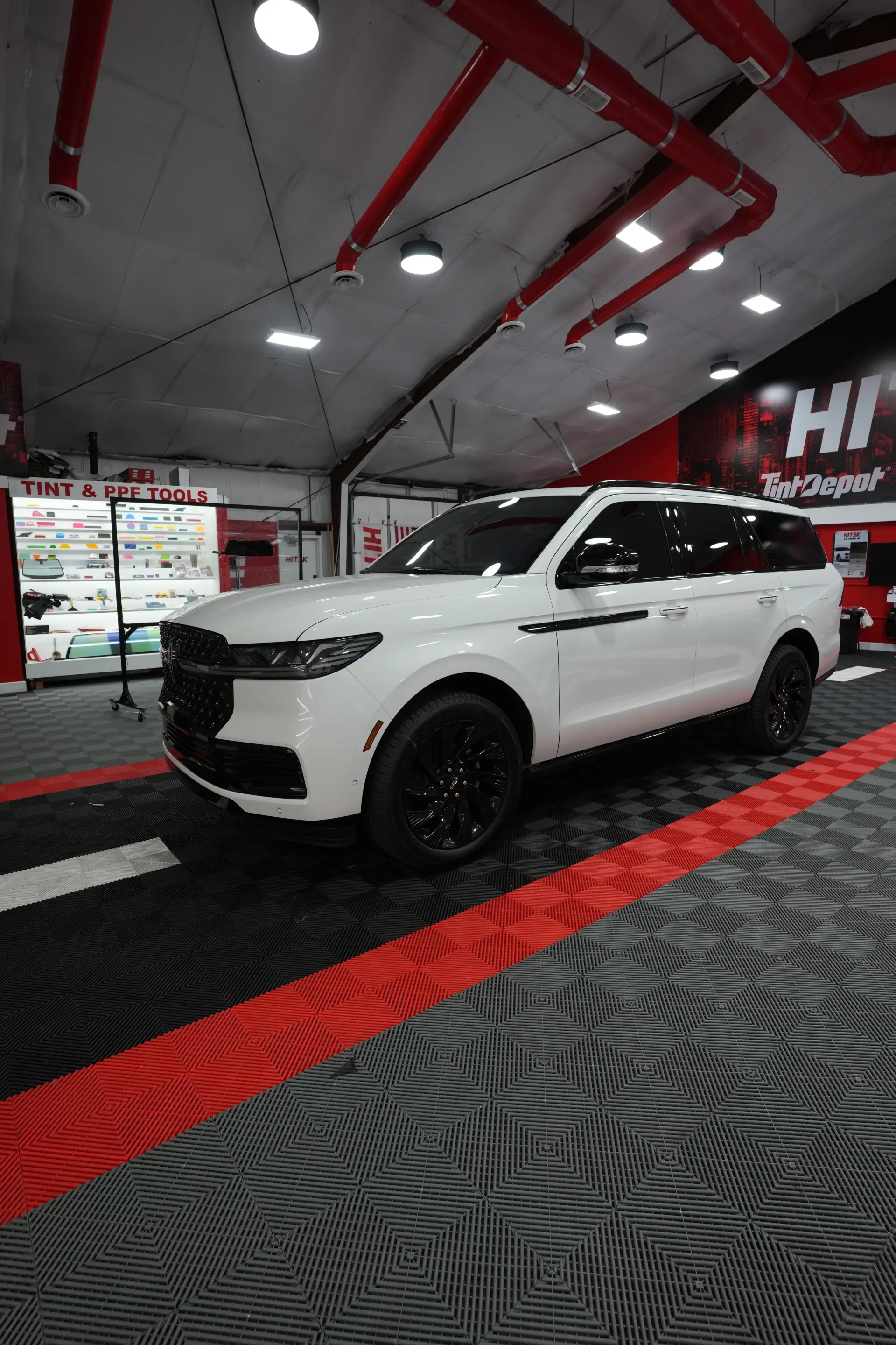 White SUV parked in a shop with red accents, black wheels, and a patterned floor.