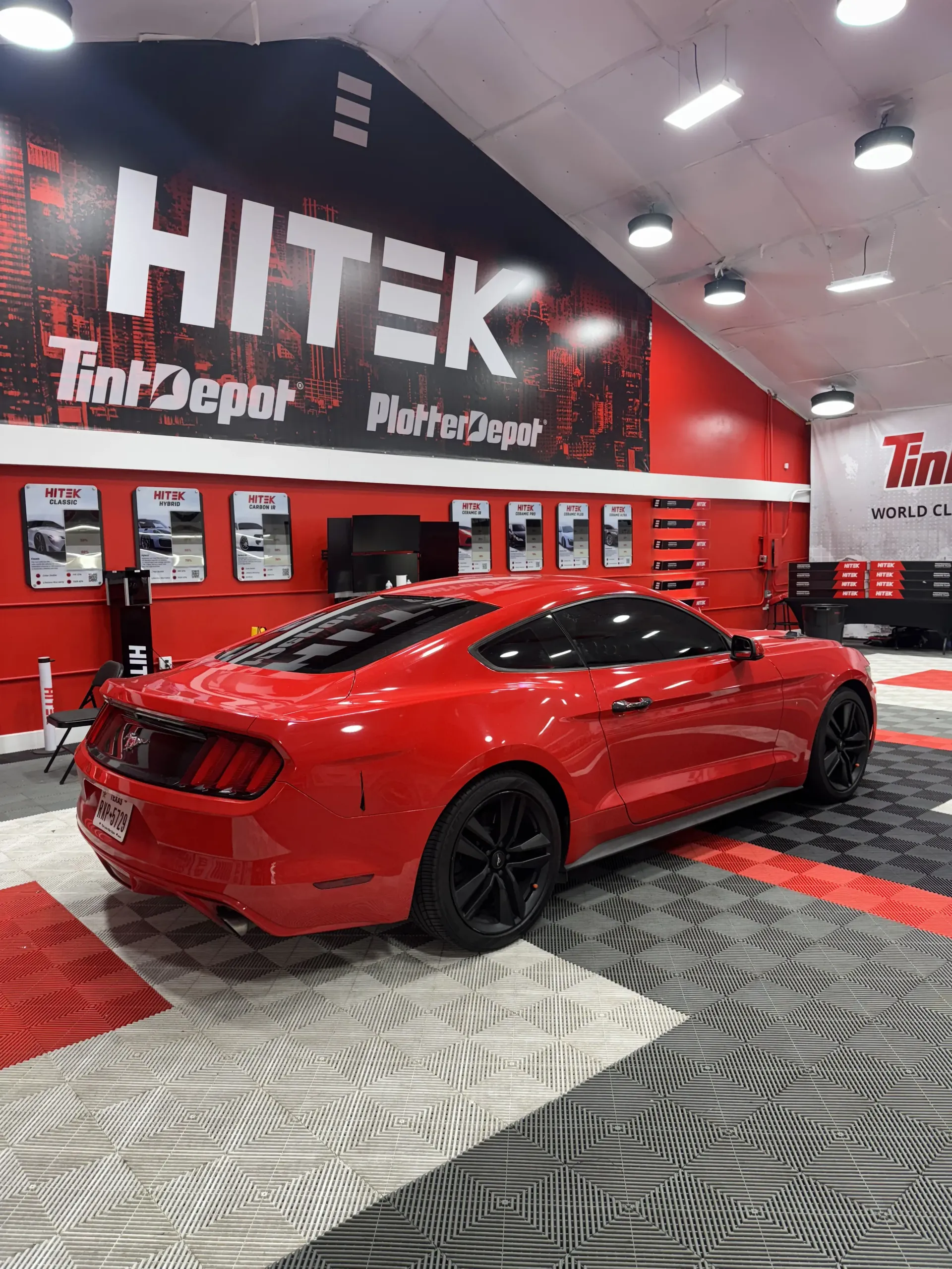 Red Ford Mustang in a car tint shop, against a red and black wall with 