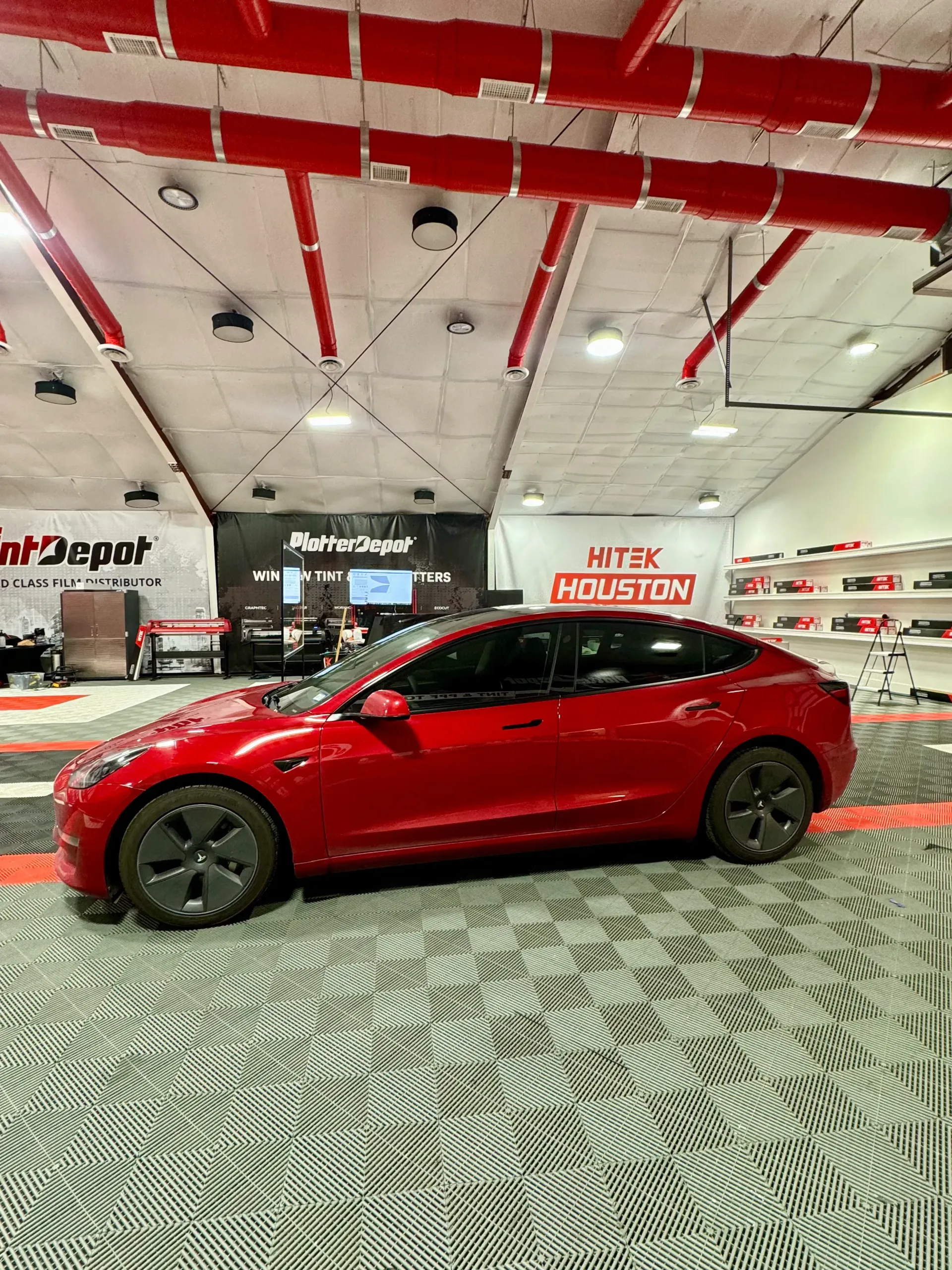 Red Tesla Model 3 inside a shop with red accents on the ceiling.