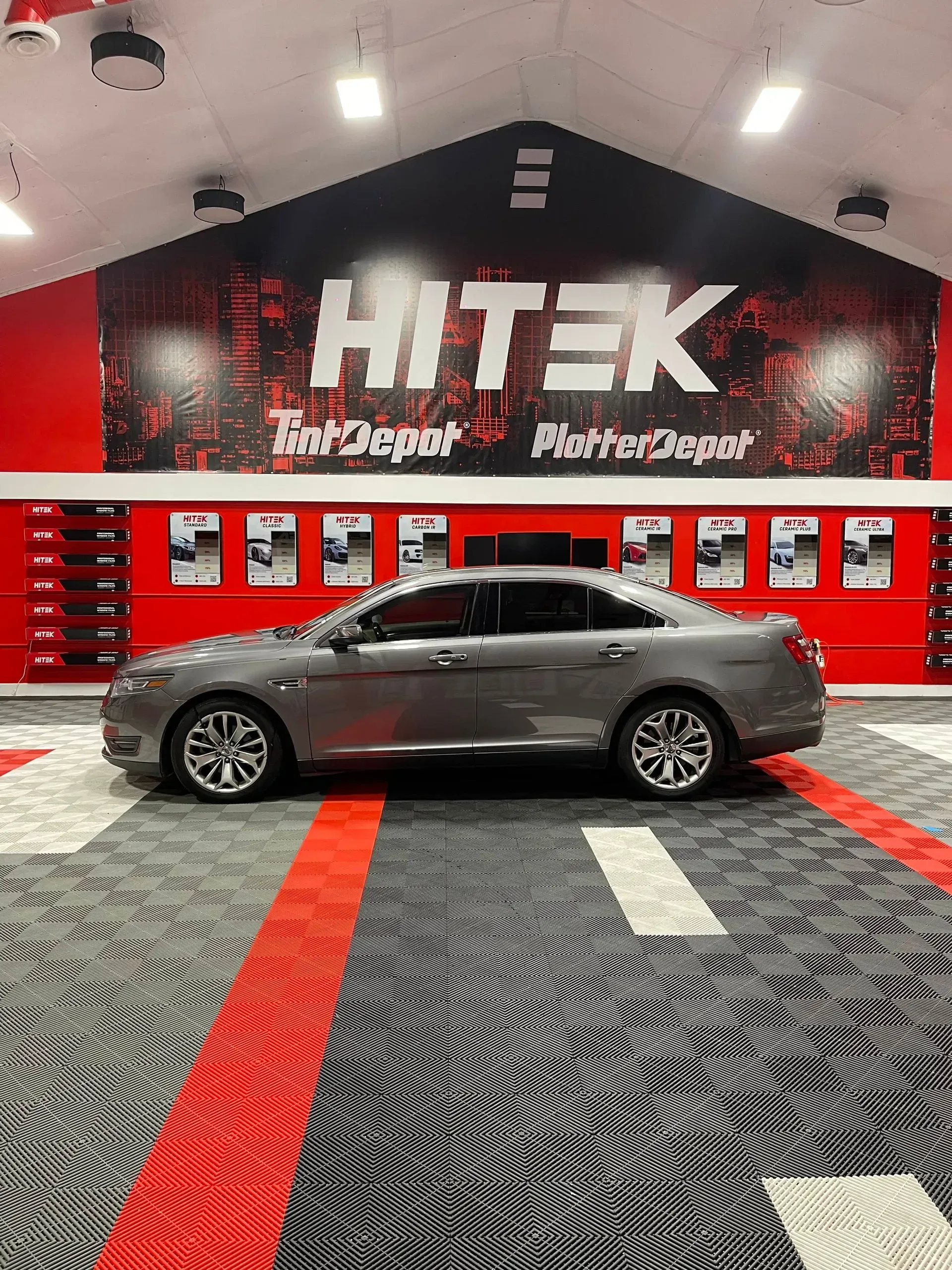 Gray sedan in a tint shop, with HiTek Tint Depot logo on the wall and red/gray floor.