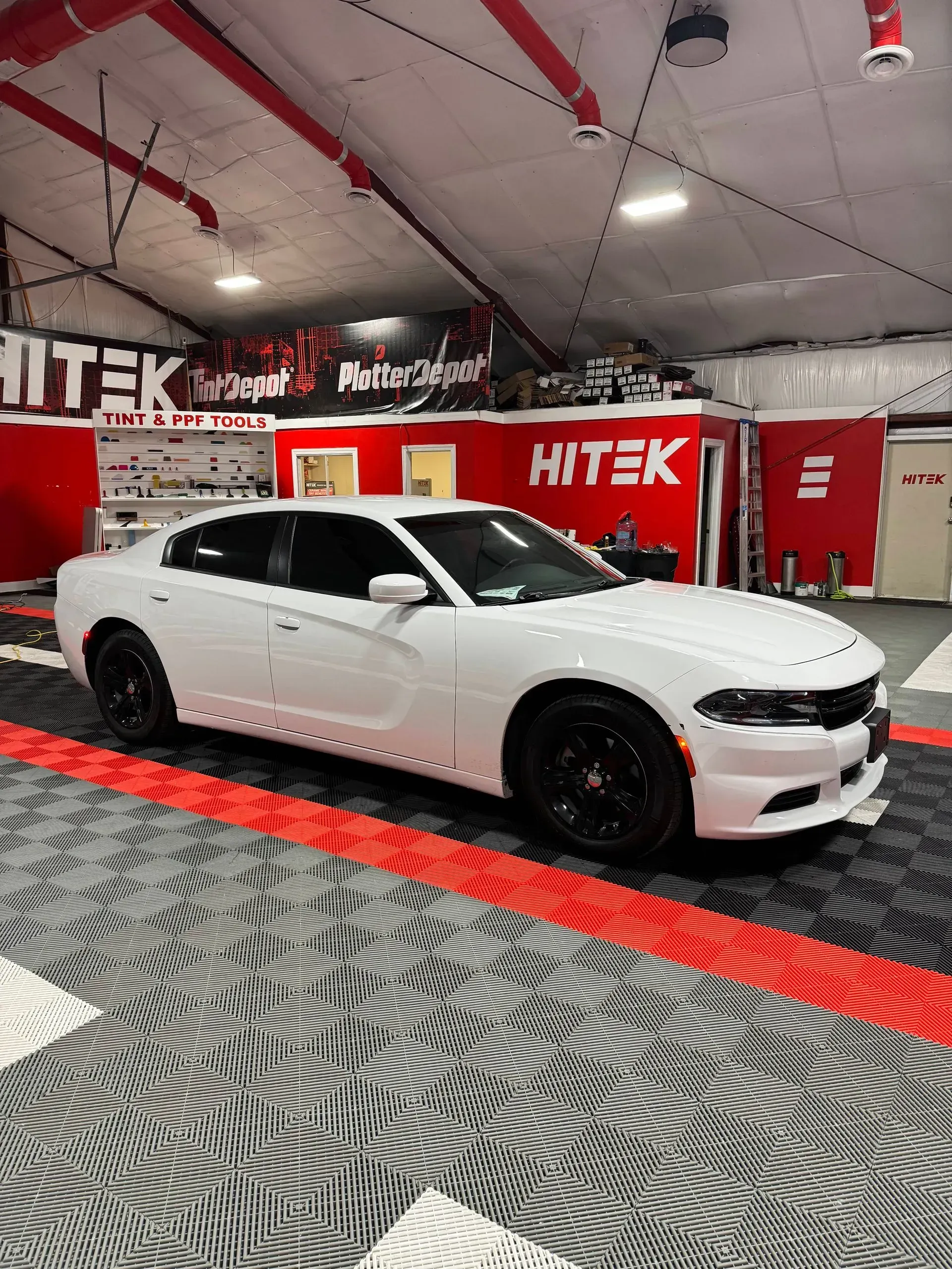 White Dodge Charger with black wheels in a garage with red accents and flooring.