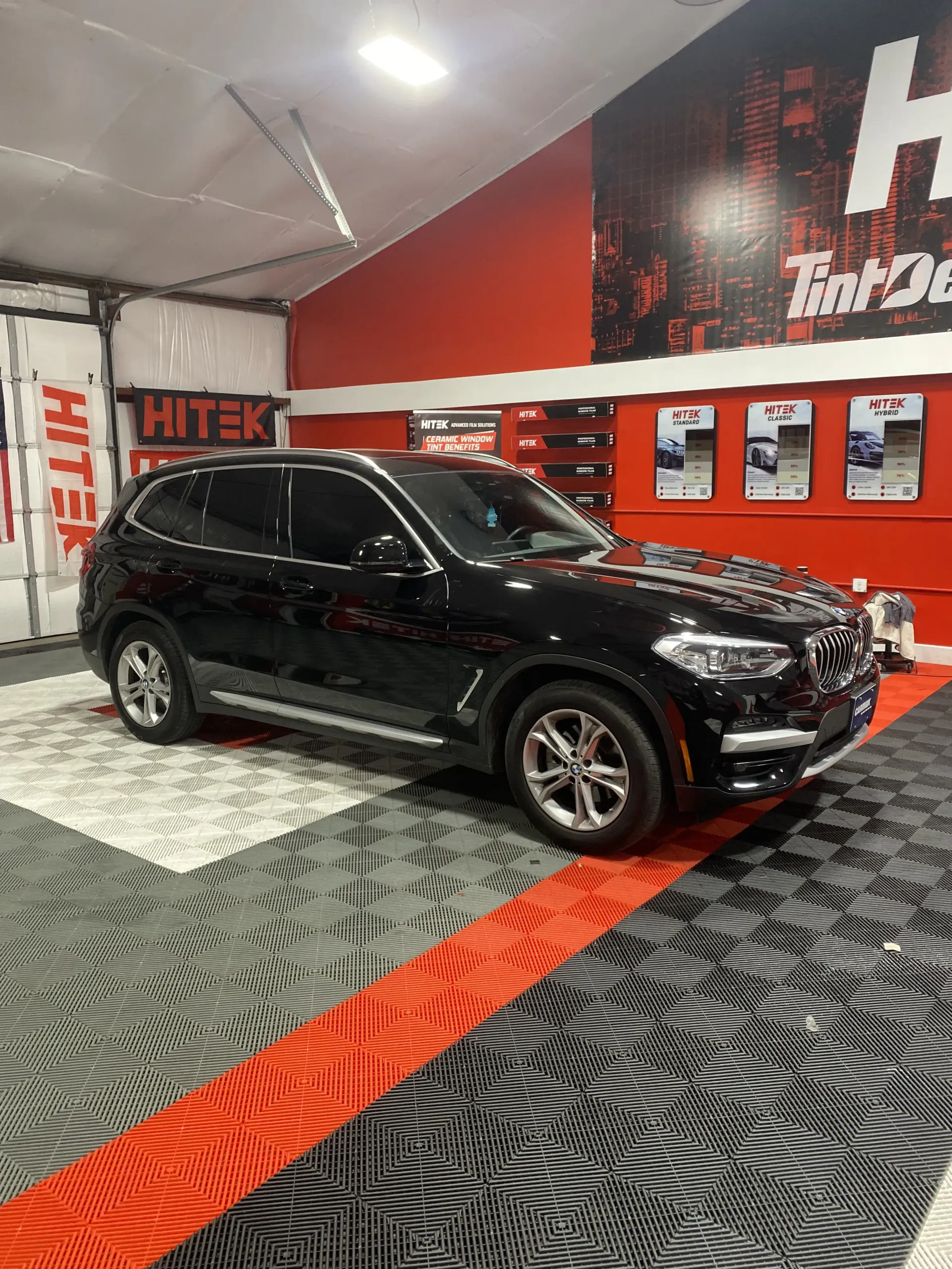 Black BMW SUV inside a tint shop. Red and white accents, patterned floor.
