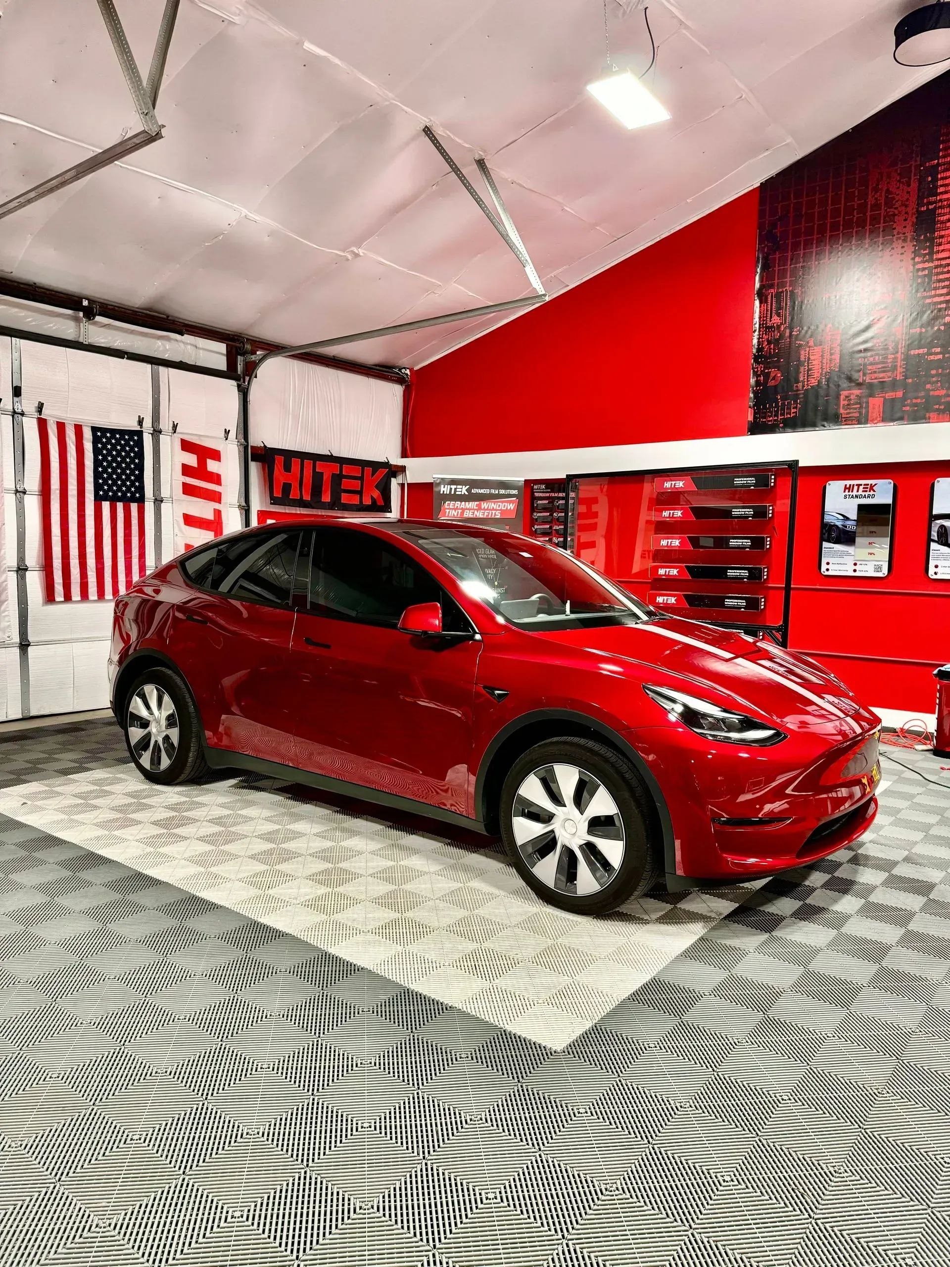 Red Tesla Y in a garage with red and white walls, an American flag, and patterned flooring.