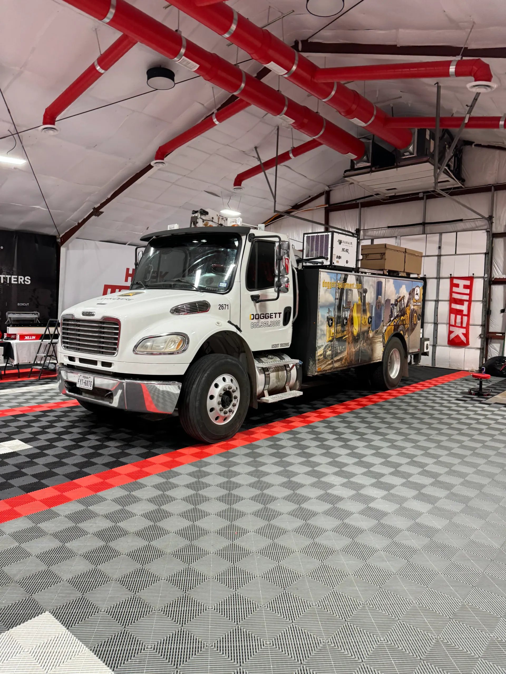 White work truck with graphics inside a garage with red accents and a patterned floor.