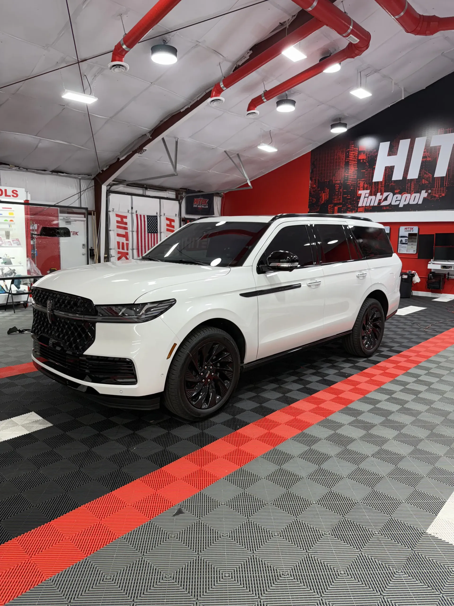 White Lincoln Navigator SUV in a shop with red accents and black wheels.