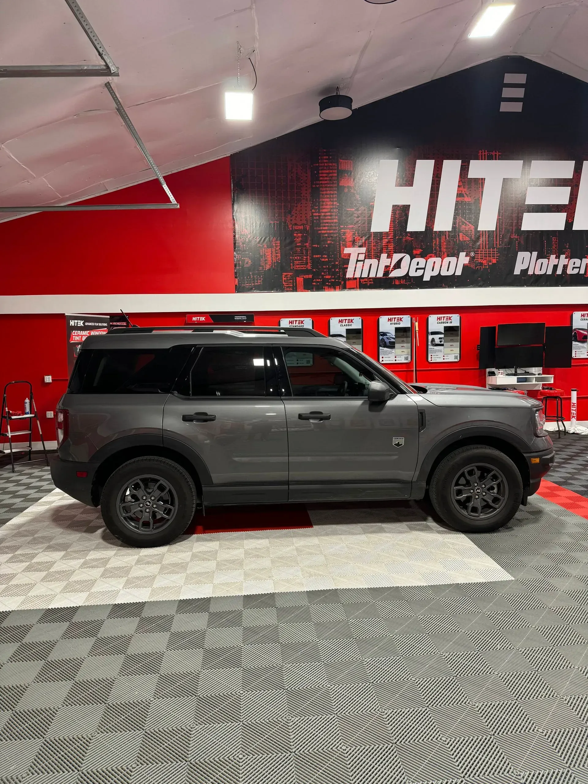 Gray Ford Bronco Sport SUV inside a red and black shop with a rug and sign.