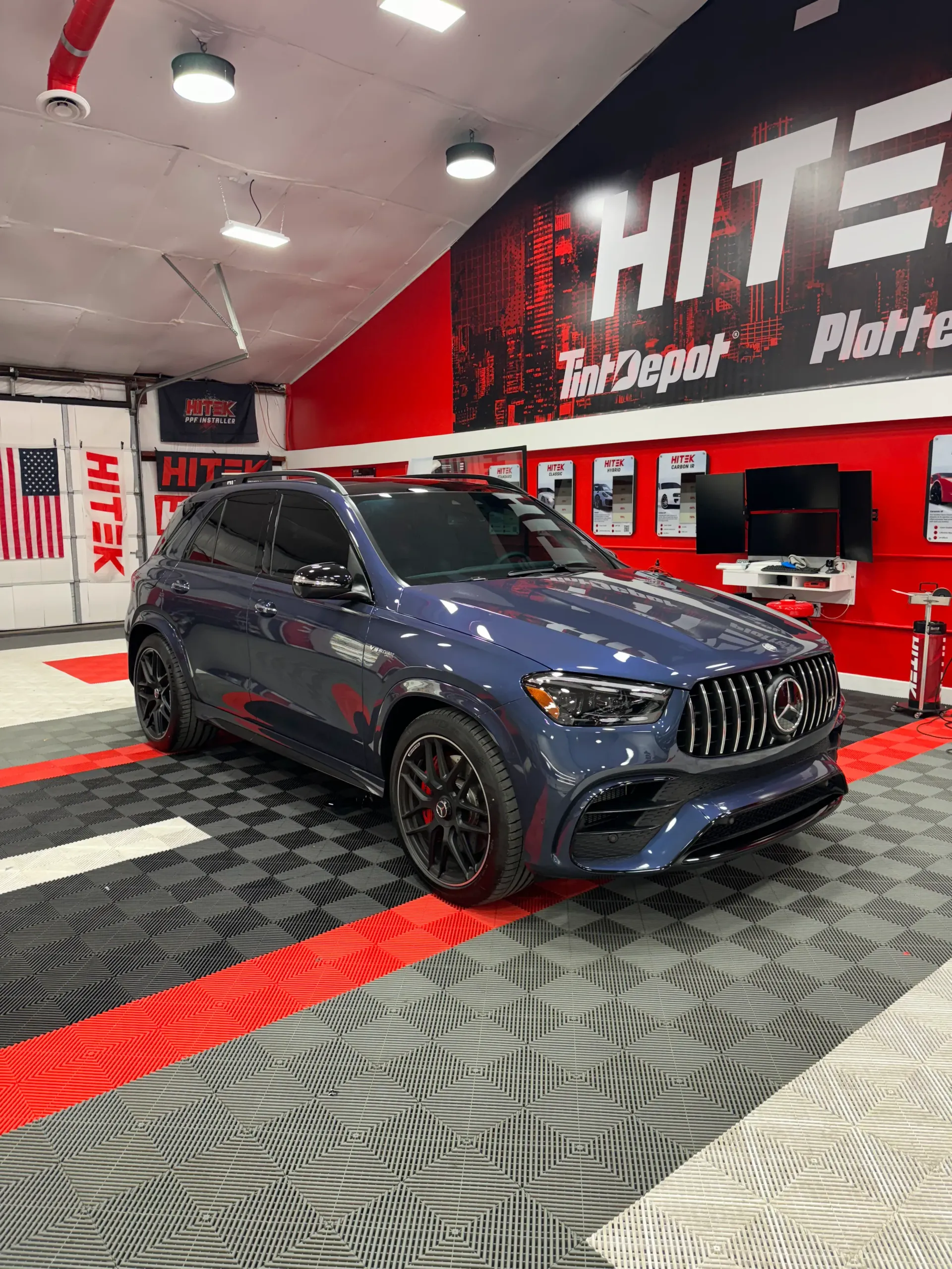 Dark blue Mercedes SUV inside a garage with red and black accents, under bright lights.