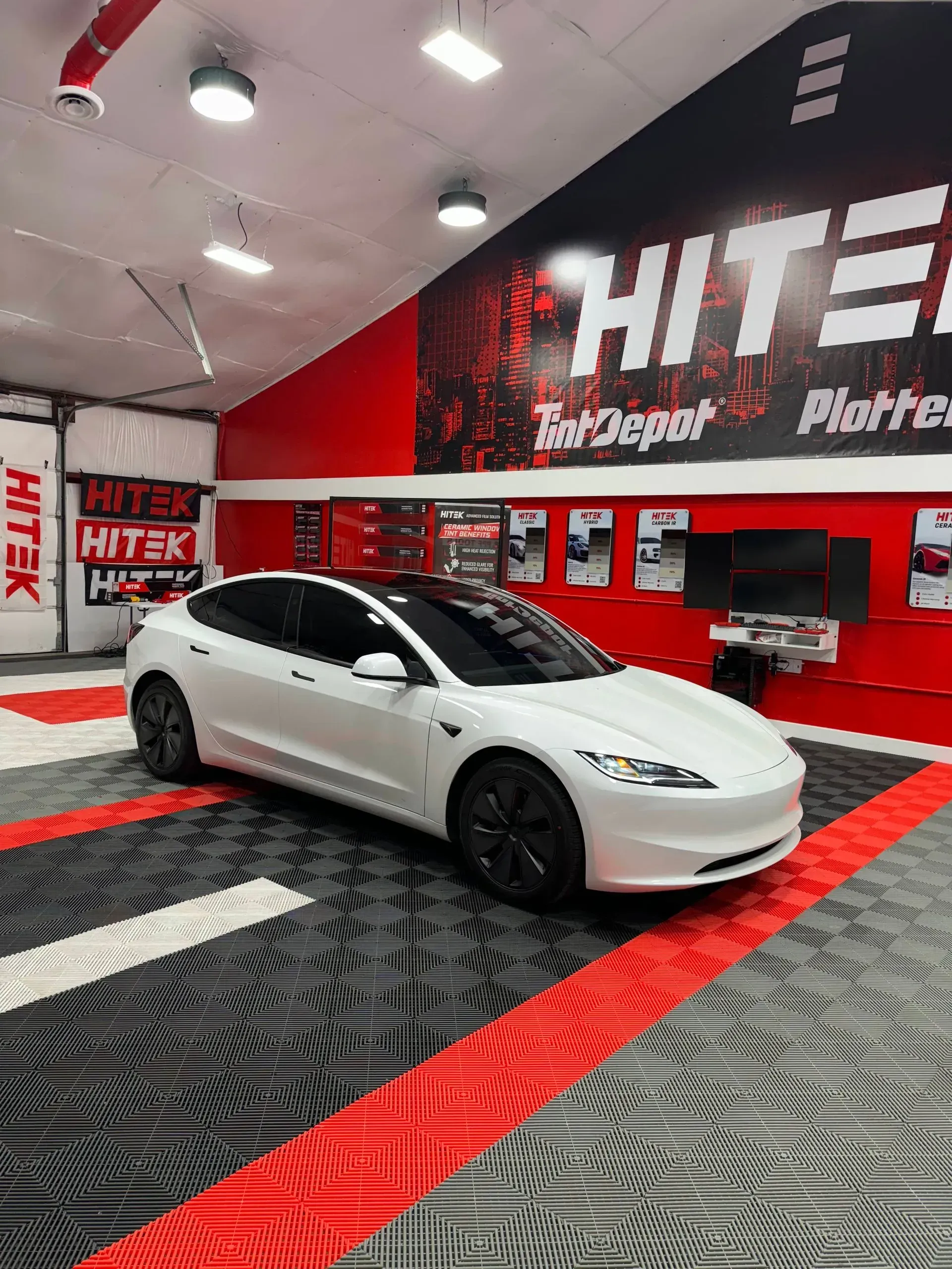 White Tesla inside a shop with red and black walls and flooring; shop sign reads 