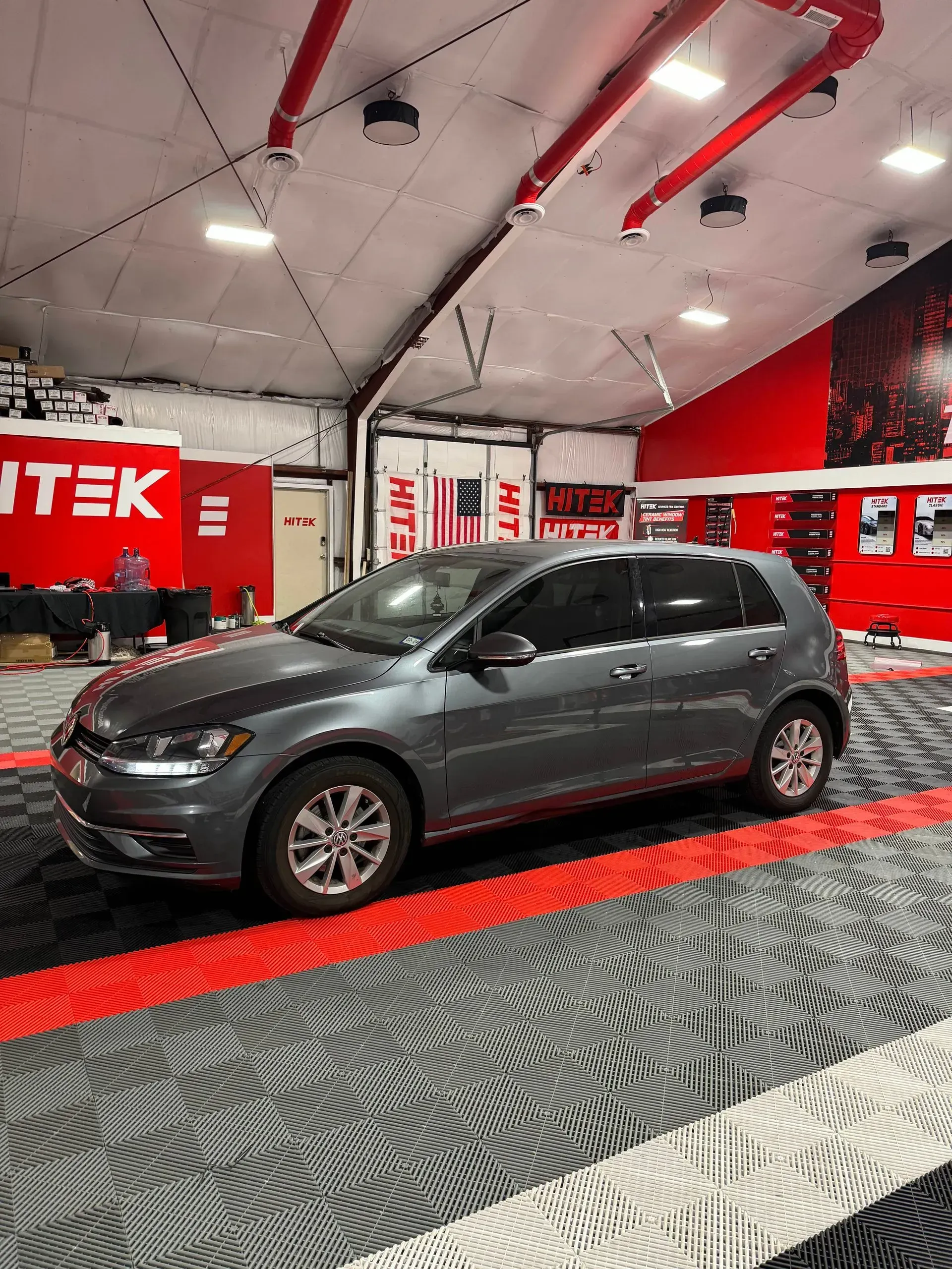 Gray Volkswagen Golf parked in a brightly lit red and white garage.