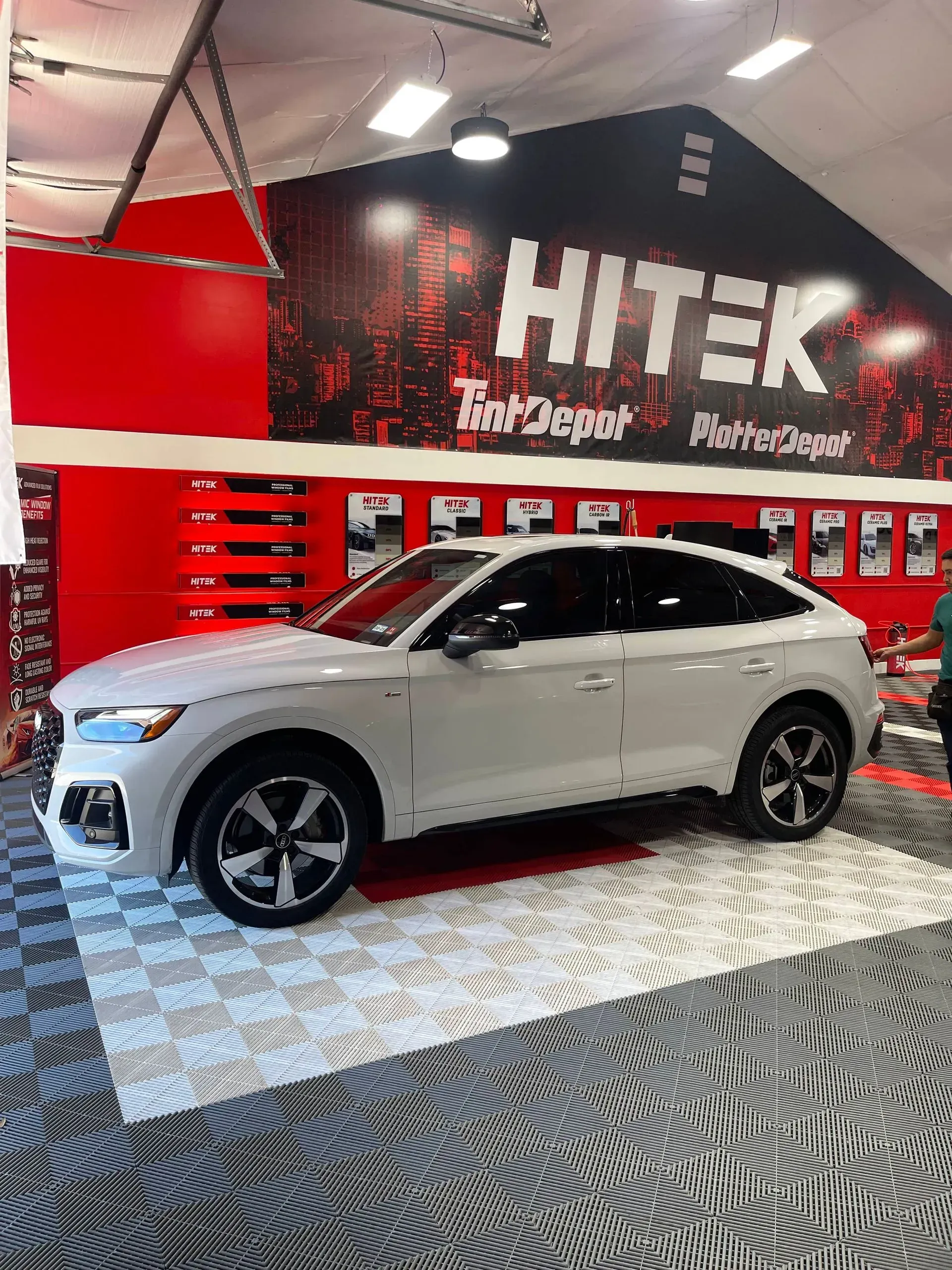 White SUV on patterned floor in front of a red and black display with the word 