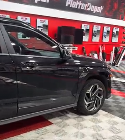 Black car parked in a red-walled shop with plotter supplies on display.