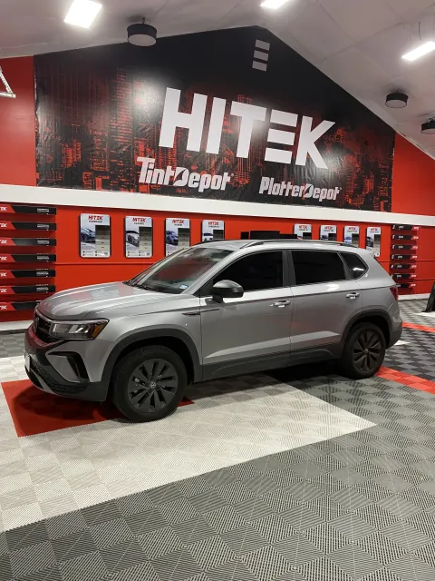 Silver SUV parked in front of a HITEK Tint Depot sign. The interior has red and black accents.