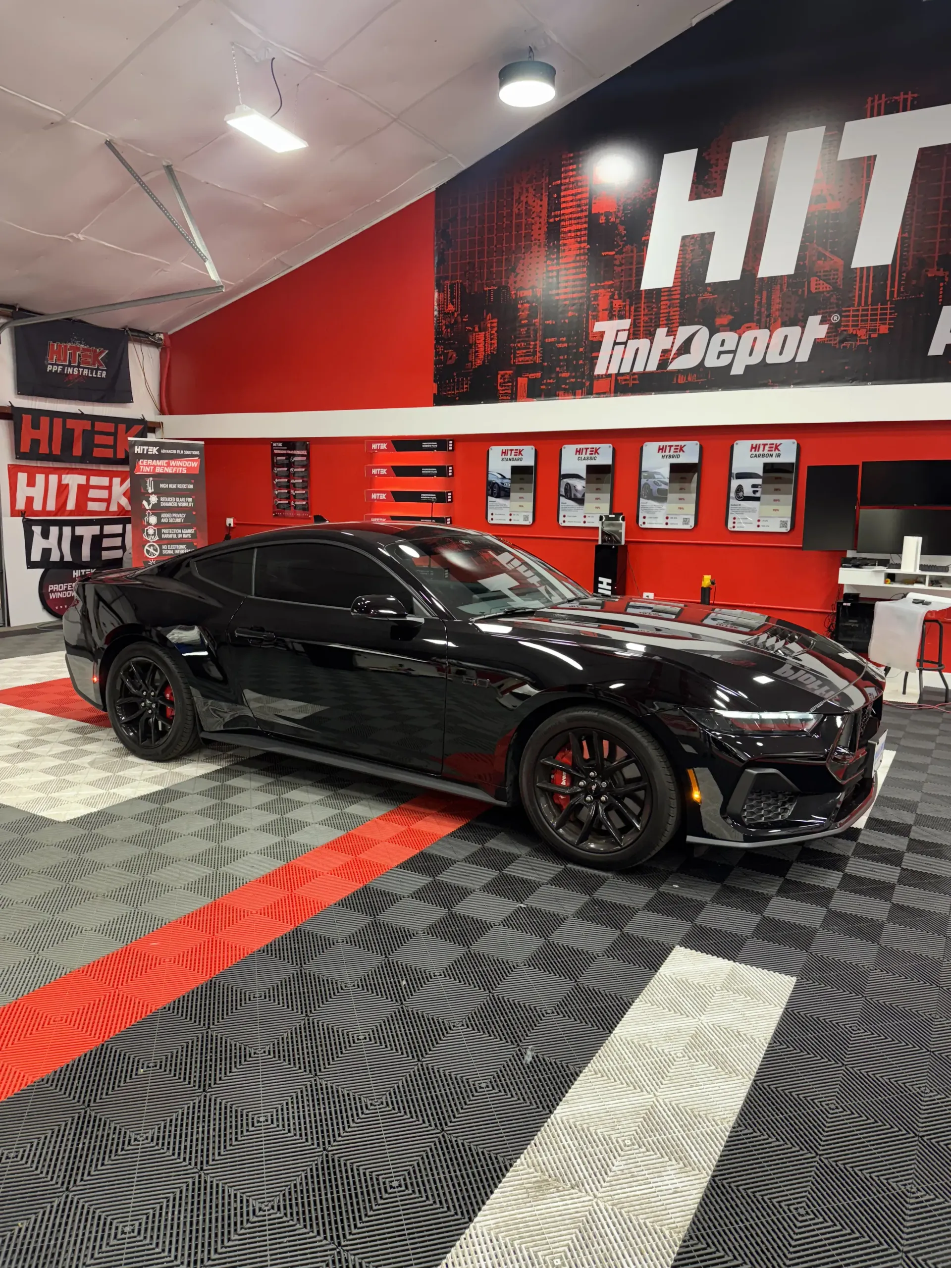 Black sports car inside a tint shop. Red and black color scheme with patterned floor.