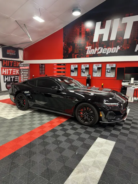 Black car inside a tint shop. Red and black decor, patterned flooring.