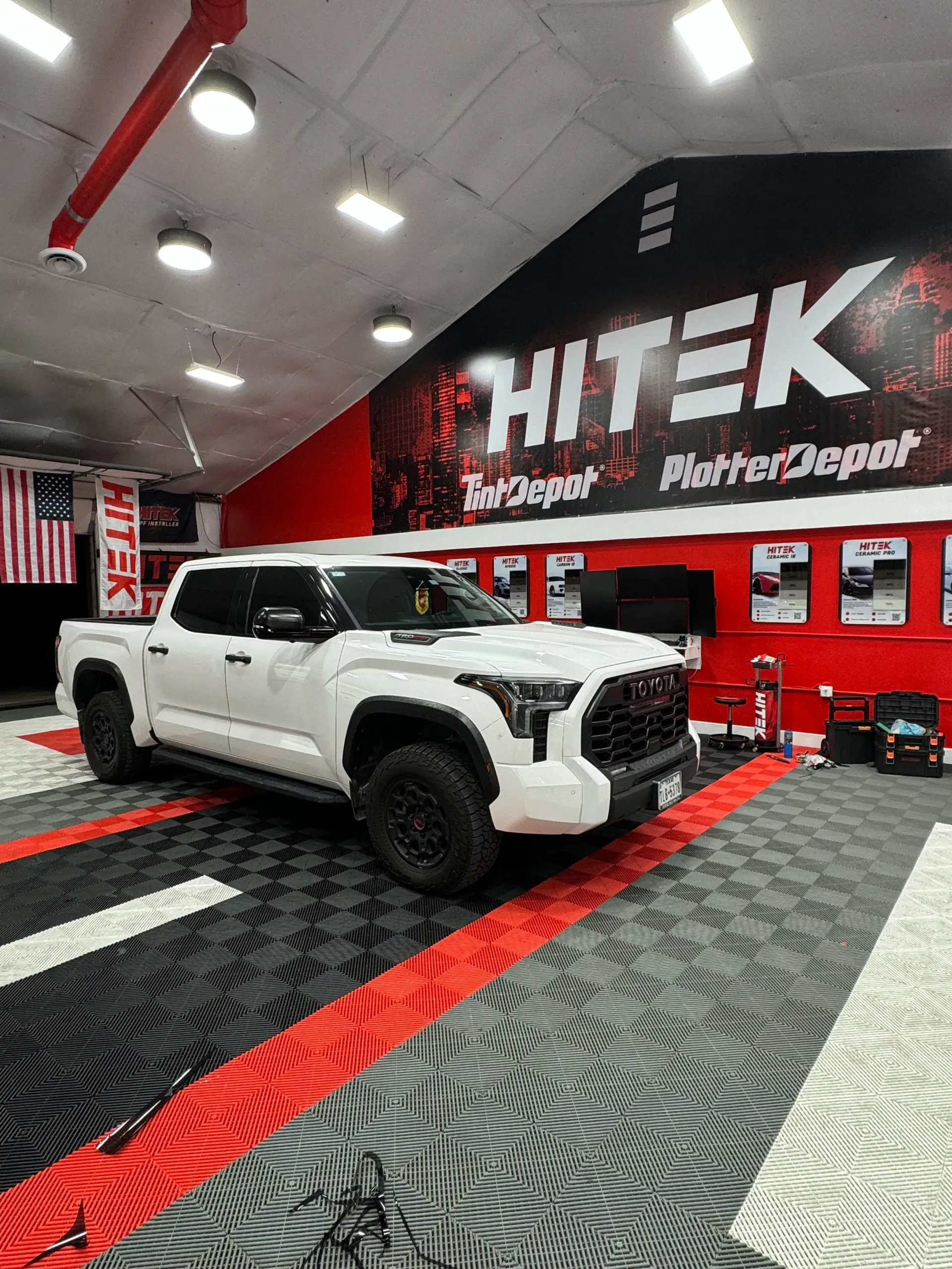 White Toyota truck parked in a garage with HI-TEK branding. Black and red tiled floor.