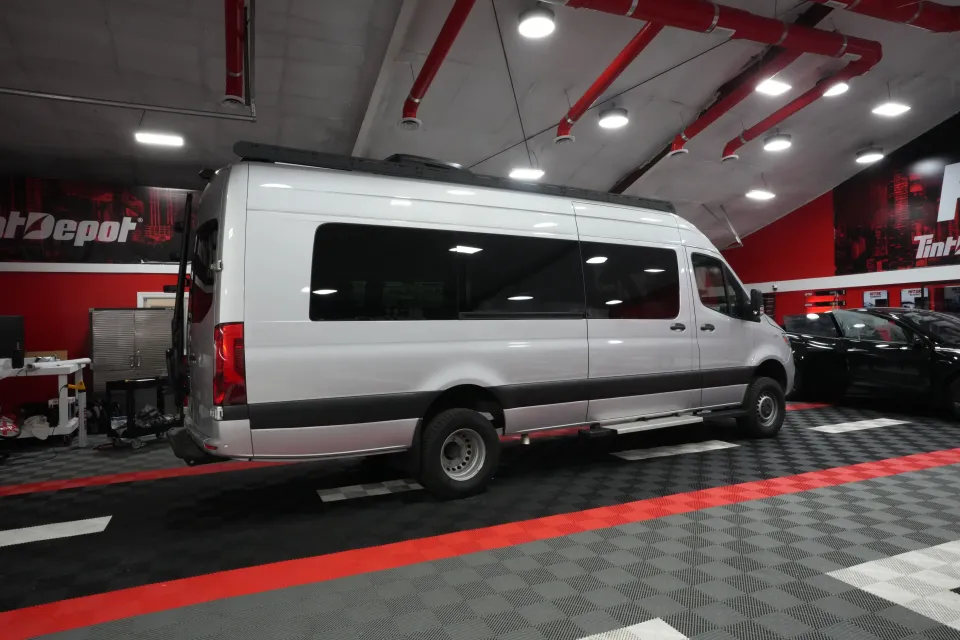 Silver van parked inside a red and black shop with overhead lighting and a black and grey patterned floor.