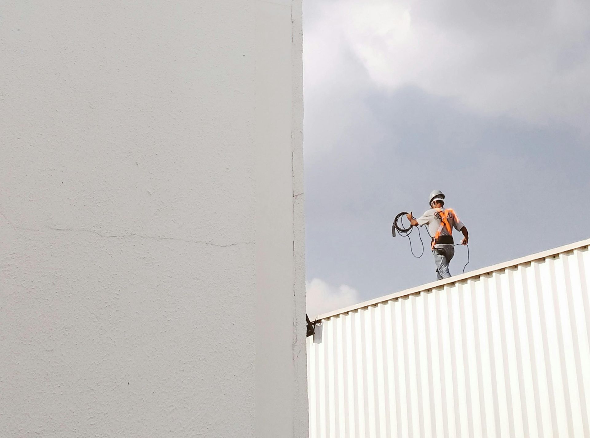 Un ouvrier sur un toit tient un outil à côté d'un haut mur blanc sous un ciel nuageux.