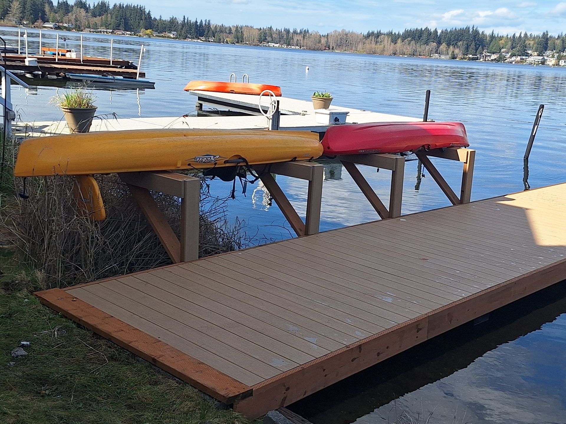Wooden dock with yellow and red kayaks on a lake, beside a small ramp and shoreline.