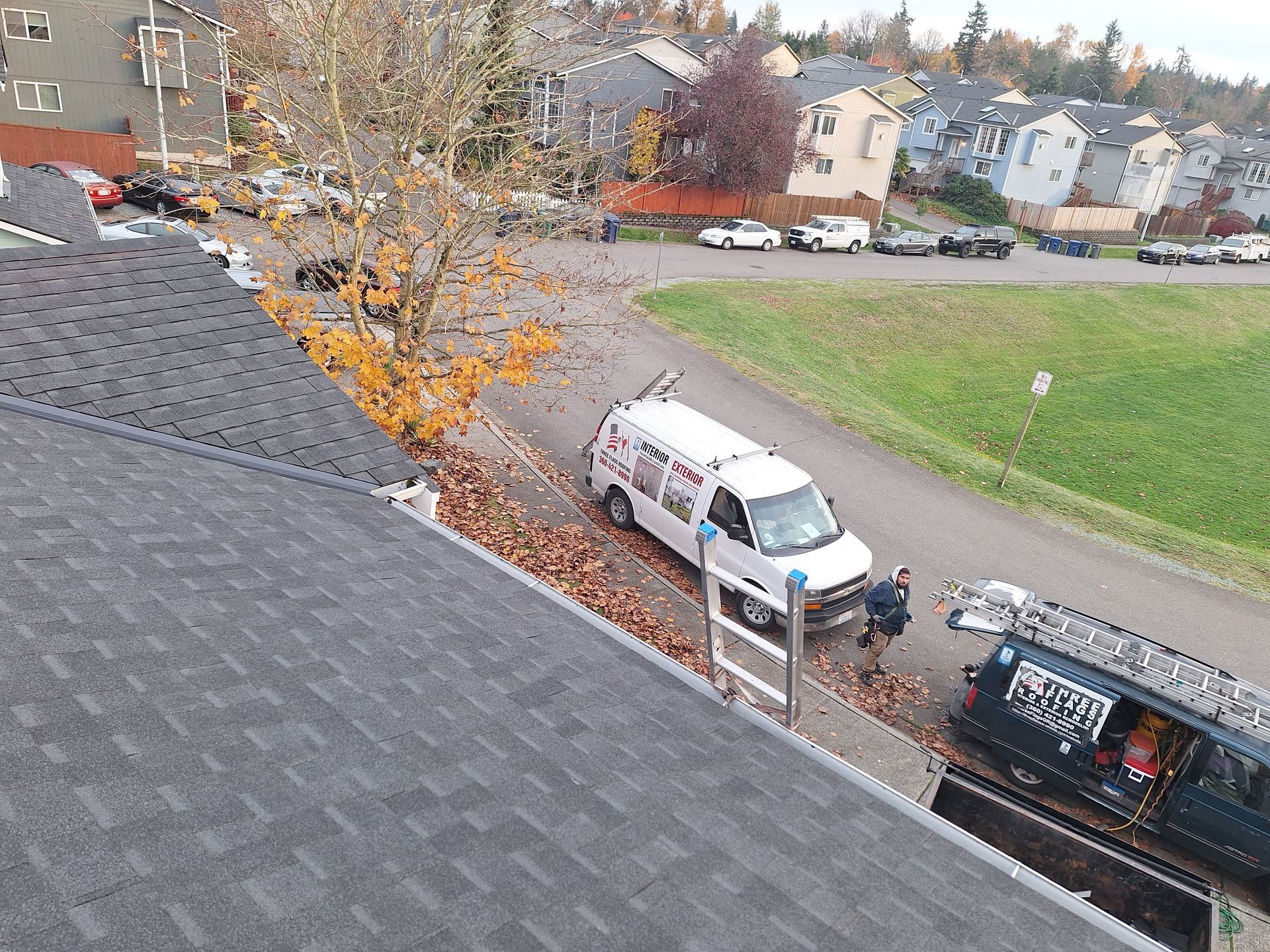 Two parked utility trucks on a residential street beside a grassy field and autumn trees.