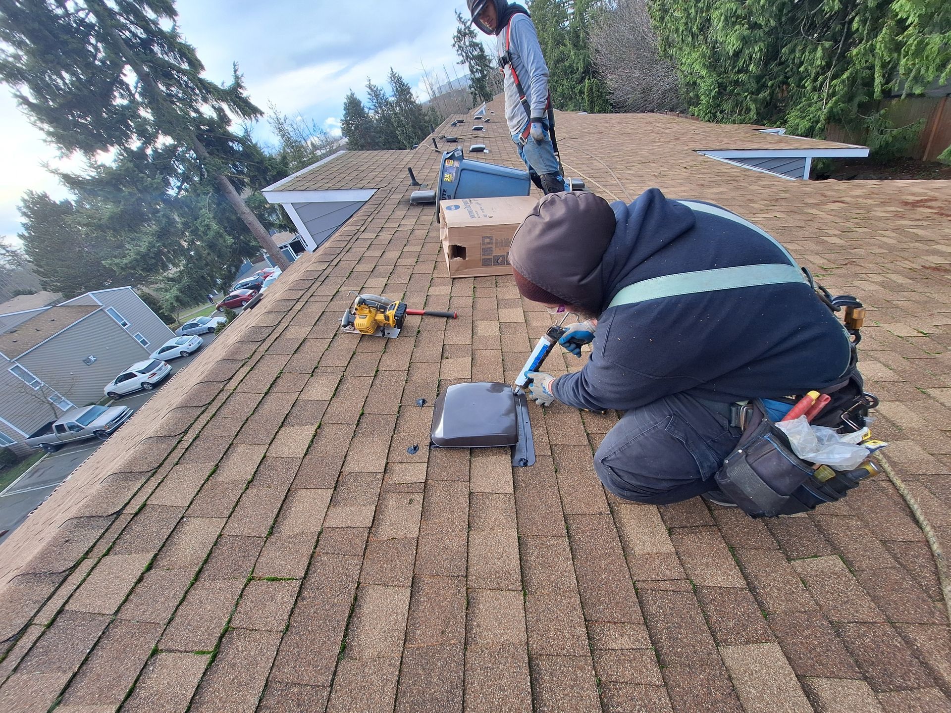Workers repairing shingles on a roof, with tools and materials spread across the brown surface.