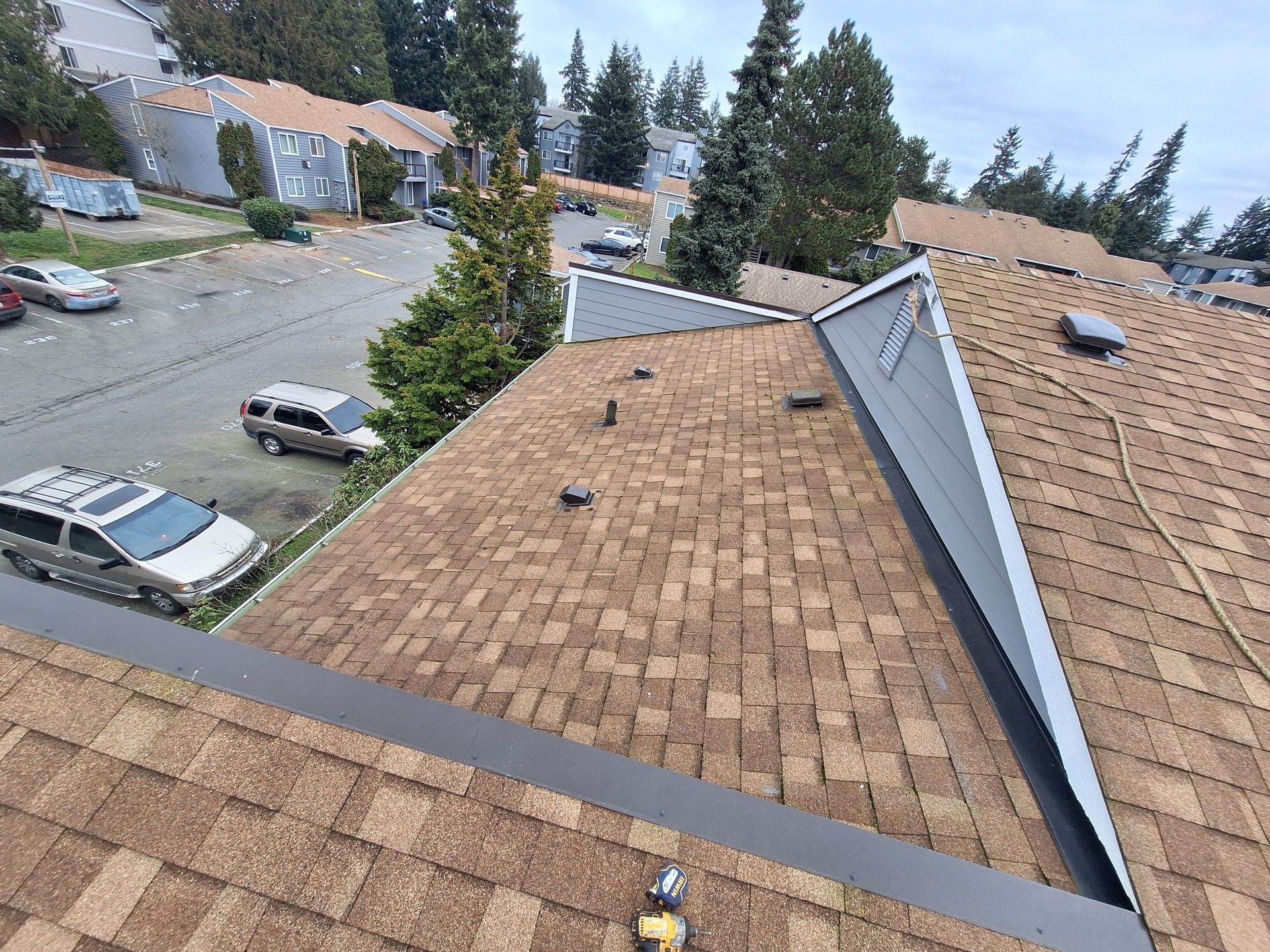 View from a roof over tan shingles and a residential street with parked cars and trees