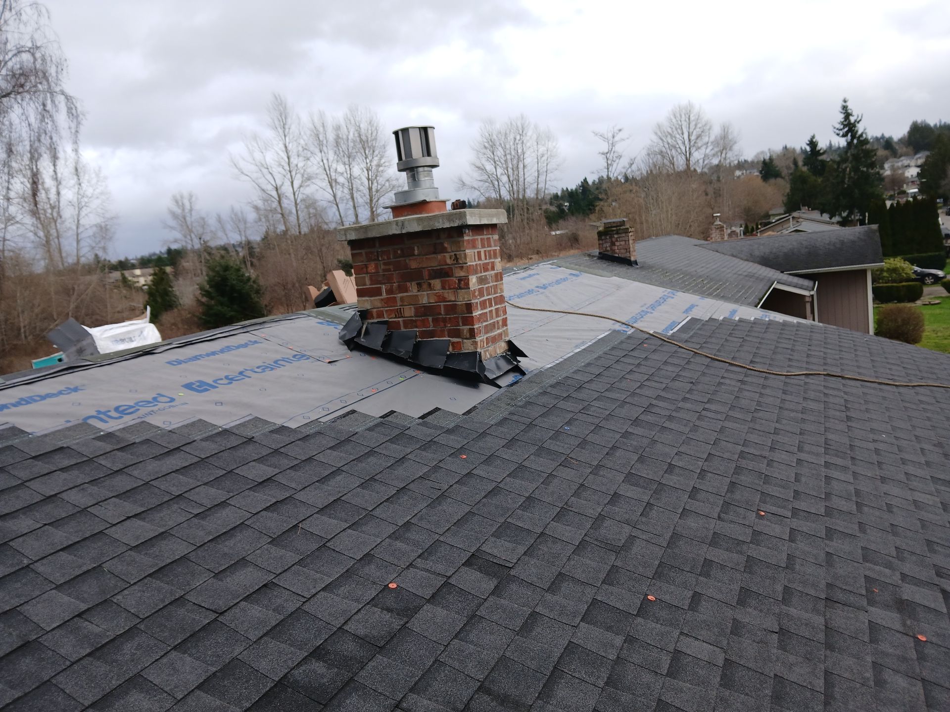 Rooftop with dark gray shingles and a brick chimney under a cloudy sky